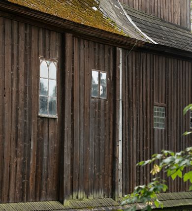 Zdjęcie nr 53: Drewniany kościół pw. św. Mikołaja w Polance jest budowlą orientowaną. Do prostokątnej nawy przylega węższe, wydłużone, trójbocznie zamknięte prezbiterium z piętrową zakrystią na osi o poligonalnym zamknięciu. Do zakrystii przylega od południa kruchta. Fragment północnej ściany prezbiterium jest murowany. Od zachodu do nawy dobudowano czworoboczną wieżę poprzedzoną przedsionkiem, który również dostawiono do nawy od południa. Prezbiterium i nawę wzniesiono na zrąb, natomiast wieżę w konstrukcji słupowej. Wieża na rzucie kwadratu posiada dwie kondygnacje. Dolna jest tej samej szerokości co nawa, górna natomiast znacznie węższa. Jej masyw podzielono smukłymi pilastrami i lizenami, zaś poniżej profilowanego gzymsu koronującego umieszczono wyrzynaną w desce koronkę. Kondygnacje oddzielono daszkiem gontowym zlewającym się po bokach z dachem kościoła. Wieżę nakryto kopulastym hełmem blaszanym, zwieńczonym blaszanym obeliskiem z krzyżem. Prezbiterium i nawę nakryto eternitowym dachem siodłowym podkreślonym profilowanym gzymsem. Nad nawą w części wschodniej zainstalowano wieżyczkę na sygnaturkę w formie wielobocznego graniastosłupa przykrytego cebulastą banią z krzyżem. Dokoła kościoła założono daszek gontowy chroniący podwaliny. Pod kościołem urządzono kryptę grzebalną. Wnętrze kościoła artykułowano za pomocą pilastrów i gzymsu. Całość nakryto stropem z fasetą. Otwór tęczowy uzyskał kształt trójlistnego, ściętego łuku, wspartego na filarkach ustawionych na profilowanej belce zawieszonej na kroksztynach. W części zachodniej nawy urządzono chór muzyczny, wsparty na dwóch kolumnach jońskich z przedpiersiem rozczłonkowanym balasami. We wnętrzu ustawiono ołtarz główny i dwa ołtarze boczne oraz ambonę, a na chórze muzycznym zainstalowano prospekt organowy.