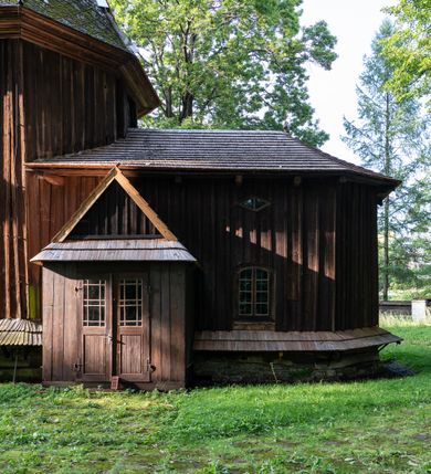 Zdjęcie nr 44: Drewniany kościół pw. św. Mikołaja w Polance jest budowlą orientowaną. Do prostokątnej nawy przylega węższe, wydłużone, trójbocznie zamknięte prezbiterium z piętrową zakrystią na osi o poligonalnym zamknięciu. Do zakrystii przylega od południa kruchta. Fragment północnej ściany prezbiterium jest murowany. Od zachodu do nawy dobudowano czworoboczną wieżę poprzedzoną przedsionkiem, który również dostawiono do nawy od południa. Prezbiterium i nawę wzniesiono na zrąb, natomiast wieżę w konstrukcji słupowej. Wieża na rzucie kwadratu posiada dwie kondygnacje. Dolna jest tej samej szerokości co nawa, górna natomiast znacznie węższa. Jej masyw podzielono smukłymi pilastrami i lizenami, zaś poniżej profilowanego gzymsu koronującego umieszczono wyrzynaną w desce koronkę. Kondygnacje oddzielono daszkiem gontowym zlewającym się po bokach z dachem kościoła. Wieżę nakryto kopulastym hełmem blaszanym, zwieńczonym blaszanym obeliskiem z krzyżem. Prezbiterium i nawę nakryto eternitowym dachem siodłowym podkreślonym profilowanym gzymsem. Nad nawą w części wschodniej zainstalowano wieżyczkę na sygnaturkę w formie wielobocznego graniastosłupa przykrytego cebulastą banią z krzyżem. Dokoła kościoła założono daszek gontowy chroniący podwaliny. Pod kościołem urządzono kryptę grzebalną. Wnętrze kościoła artykułowano za pomocą pilastrów i gzymsu. Całość nakryto stropem z fasetą. Otwór tęczowy uzyskał kształt trójlistnego, ściętego łuku, wspartego na filarkach ustawionych na profilowanej belce zawieszonej na kroksztynach. W części zachodniej nawy urządzono chór muzyczny, wsparty na dwóch kolumnach jońskich z przedpiersiem rozczłonkowanym balasami. We wnętrzu ustawiono ołtarz główny i dwa ołtarze boczne oraz ambonę, a na chórze muzycznym zainstalowano prospekt organowy.