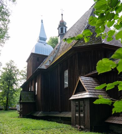 Zdjęcie nr 42: Drewniany kościół pw. św. Mikołaja w Polance jest budowlą orientowaną. Do prostokątnej nawy przylega węższe, wydłużone, trójbocznie zamknięte prezbiterium z piętrową zakrystią na osi o poligonalnym zamknięciu. Do zakrystii przylega od południa kruchta. Fragment północnej ściany prezbiterium jest murowany. Od zachodu do nawy dobudowano czworoboczną wieżę poprzedzoną przedsionkiem, który również dostawiono do nawy od południa. Prezbiterium i nawę wzniesiono na zrąb, natomiast wieżę w konstrukcji słupowej. Wieża na rzucie kwadratu posiada dwie kondygnacje. Dolna jest tej samej szerokości co nawa, górna natomiast znacznie węższa. Jej masyw podzielono smukłymi pilastrami i lizenami, zaś poniżej profilowanego gzymsu koronującego umieszczono wyrzynaną w desce koronkę. Kondygnacje oddzielono daszkiem gontowym zlewającym się po bokach z dachem kościoła. Wieżę nakryto kopulastym hełmem blaszanym, zwieńczonym blaszanym obeliskiem z krzyżem. Prezbiterium i nawę nakryto eternitowym dachem siodłowym podkreślonym profilowanym gzymsem. Nad nawą w części wschodniej zainstalowano wieżyczkę na sygnaturkę w formie wielobocznego graniastosłupa przykrytego cebulastą banią z krzyżem. Dokoła kościoła założono daszek gontowy chroniący podwaliny. Pod kościołem urządzono kryptę grzebalną. Wnętrze kościoła artykułowano za pomocą pilastrów i gzymsu. Całość nakryto stropem z fasetą. Otwór tęczowy uzyskał kształt trójlistnego, ściętego łuku, wspartego na filarkach ustawionych na profilowanej belce zawieszonej na kroksztynach. W części zachodniej nawy urządzono chór muzyczny, wsparty na dwóch kolumnach jońskich z przedpiersiem rozczłonkowanym balasami. We wnętrzu ustawiono ołtarz główny i dwa ołtarze boczne oraz ambonę, a na chórze muzycznym zainstalowano prospekt organowy.