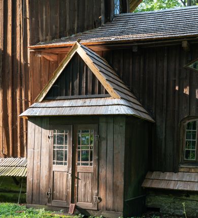 Zdjęcie nr 50: Drewniany kościół pw. św. Mikołaja w Polance jest budowlą orientowaną. Do prostokątnej nawy przylega węższe, wydłużone, trójbocznie zamknięte prezbiterium z piętrową zakrystią na osi o poligonalnym zamknięciu. Do zakrystii przylega od południa kruchta. Fragment północnej ściany prezbiterium jest murowany. Od zachodu do nawy dobudowano czworoboczną wieżę poprzedzoną przedsionkiem, który również dostawiono do nawy od południa. Prezbiterium i nawę wzniesiono na zrąb, natomiast wieżę w konstrukcji słupowej. Wieża na rzucie kwadratu posiada dwie kondygnacje. Dolna jest tej samej szerokości co nawa, górna natomiast znacznie węższa. Jej masyw podzielono smukłymi pilastrami i lizenami, zaś poniżej profilowanego gzymsu koronującego umieszczono wyrzynaną w desce koronkę. Kondygnacje oddzielono daszkiem gontowym zlewającym się po bokach z dachem kościoła. Wieżę nakryto kopulastym hełmem blaszanym, zwieńczonym blaszanym obeliskiem z krzyżem. Prezbiterium i nawę nakryto eternitowym dachem siodłowym podkreślonym profilowanym gzymsem. Nad nawą w części wschodniej zainstalowano wieżyczkę na sygnaturkę w formie wielobocznego graniastosłupa przykrytego cebulastą banią z krzyżem. Dokoła kościoła założono daszek gontowy chroniący podwaliny. Pod kościołem urządzono kryptę grzebalną. Wnętrze kościoła artykułowano za pomocą pilastrów i gzymsu. Całość nakryto stropem z fasetą. Otwór tęczowy uzyskał kształt trójlistnego, ściętego łuku, wspartego na filarkach ustawionych na profilowanej belce zawieszonej na kroksztynach. W części zachodniej nawy urządzono chór muzyczny, wsparty na dwóch kolumnach jońskich z przedpiersiem rozczłonkowanym balasami. We wnętrzu ustawiono ołtarz główny i dwa ołtarze boczne oraz ambonę, a na chórze muzycznym zainstalowano prospekt organowy.