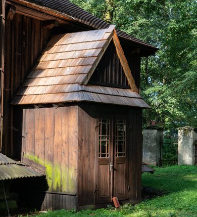Zdjęcie nr 35: Drewniany kościół pw. św. Mikołaja w Polance jest budowlą orientowaną. Do prostokątnej nawy przylega węższe, wydłużone, trójbocznie zamknięte prezbiterium z piętrową zakrystią na osi o poligonalnym zamknięciu. Do zakrystii przylega od południa kruchta. Fragment północnej ściany prezbiterium jest murowany. Od zachodu do nawy dobudowano czworoboczną wieżę poprzedzoną przedsionkiem, który również dostawiono do nawy od południa. Prezbiterium i nawę wzniesiono na zrąb, natomiast wieżę w konstrukcji słupowej. Wieża na rzucie kwadratu posiada dwie kondygnacje. Dolna jest tej samej szerokości co nawa, górna natomiast znacznie węższa. Jej masyw podzielono smukłymi pilastrami i lizenami, zaś poniżej profilowanego gzymsu koronującego umieszczono wyrzynaną w desce koronkę. Kondygnacje oddzielono daszkiem gontowym zlewającym się po bokach z dachem kościoła. Wieżę nakryto kopulastym hełmem blaszanym, zwieńczonym blaszanym obeliskiem z krzyżem. Prezbiterium i nawę nakryto eternitowym dachem siodłowym podkreślonym profilowanym gzymsem. Nad nawą w części wschodniej zainstalowano wieżyczkę na sygnaturkę w formie wielobocznego graniastosłupa przykrytego cebulastą banią z krzyżem. Dokoła kościoła założono daszek gontowy chroniący podwaliny. Pod kościołem urządzono kryptę grzebalną. Wnętrze kościoła artykułowano za pomocą pilastrów i gzymsu. Całość nakryto stropem z fasetą. Otwór tęczowy uzyskał kształt trójlistnego, ściętego łuku, wspartego na filarkach ustawionych na profilowanej belce zawieszonej na kroksztynach. W części zachodniej nawy urządzono chór muzyczny, wsparty na dwóch kolumnach jońskich z przedpiersiem rozczłonkowanym balasami. We wnętrzu ustawiono ołtarz główny i dwa ołtarze boczne oraz ambonę, a na chórze muzycznym zainstalowano prospekt organowy.