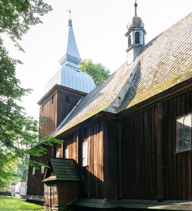 Zdjęcie nr 43: Drewniany kościół pw. św. Mikołaja w Polance jest budowlą orientowaną. Do prostokątnej nawy przylega węższe, wydłużone, trójbocznie zamknięte prezbiterium z piętrową zakrystią na osi o poligonalnym zamknięciu. Do zakrystii przylega od południa kruchta. Fragment północnej ściany prezbiterium jest murowany. Od zachodu do nawy dobudowano czworoboczną wieżę poprzedzoną przedsionkiem, który również dostawiono do nawy od południa. Prezbiterium i nawę wzniesiono na zrąb, natomiast wieżę w konstrukcji słupowej. Wieża na rzucie kwadratu posiada dwie kondygnacje. Dolna jest tej samej szerokości co nawa, górna natomiast znacznie węższa. Jej masyw podzielono smukłymi pilastrami i lizenami, zaś poniżej profilowanego gzymsu koronującego umieszczono wyrzynaną w desce koronkę. Kondygnacje oddzielono daszkiem gontowym zlewającym się po bokach z dachem kościoła. Wieżę nakryto kopulastym hełmem blaszanym, zwieńczonym blaszanym obeliskiem z krzyżem. Prezbiterium i nawę nakryto eternitowym dachem siodłowym podkreślonym profilowanym gzymsem. Nad nawą w części wschodniej zainstalowano wieżyczkę na sygnaturkę w formie wielobocznego graniastosłupa przykrytego cebulastą banią z krzyżem. Dokoła kościoła założono daszek gontowy chroniący podwaliny. Pod kościołem urządzono kryptę grzebalną. Wnętrze kościoła artykułowano za pomocą pilastrów i gzymsu. Całość nakryto stropem z fasetą. Otwór tęczowy uzyskał kształt trójlistnego, ściętego łuku, wspartego na filarkach ustawionych na profilowanej belce zawieszonej na kroksztynach. W części zachodniej nawy urządzono chór muzyczny, wsparty na dwóch kolumnach jońskich z przedpiersiem rozczłonkowanym balasami. We wnętrzu ustawiono ołtarz główny i dwa ołtarze boczne oraz ambonę, a na chórze muzycznym zainstalowano prospekt organowy.