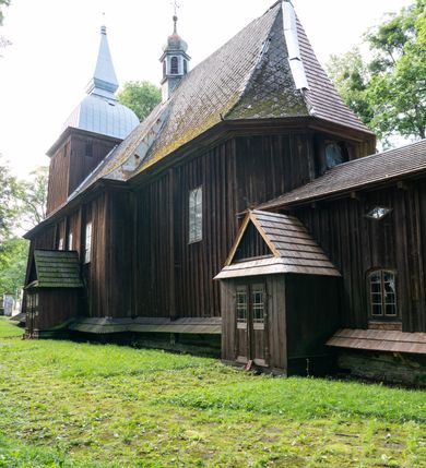 Zdjęcie nr 47: Drewniany kościół pw. św. Mikołaja w Polance jest budowlą orientowaną. Do prostokątnej nawy przylega węższe, wydłużone, trójbocznie zamknięte prezbiterium z piętrową zakrystią na osi o poligonalnym zamknięciu. Do zakrystii przylega od południa kruchta. Fragment północnej ściany prezbiterium jest murowany. Od zachodu do nawy dobudowano czworoboczną wieżę poprzedzoną przedsionkiem, który również dostawiono do nawy od południa. Prezbiterium i nawę wzniesiono na zrąb, natomiast wieżę w konstrukcji słupowej. Wieża na rzucie kwadratu posiada dwie kondygnacje. Dolna jest tej samej szerokości co nawa, górna natomiast znacznie węższa. Jej masyw podzielono smukłymi pilastrami i lizenami, zaś poniżej profilowanego gzymsu koronującego umieszczono wyrzynaną w desce koronkę. Kondygnacje oddzielono daszkiem gontowym zlewającym się po bokach z dachem kościoła. Wieżę nakryto kopulastym hełmem blaszanym, zwieńczonym blaszanym obeliskiem z krzyżem. Prezbiterium i nawę nakryto eternitowym dachem siodłowym podkreślonym profilowanym gzymsem. Nad nawą w części wschodniej zainstalowano wieżyczkę na sygnaturkę w formie wielobocznego graniastosłupa przykrytego cebulastą banią z krzyżem. Dokoła kościoła założono daszek gontowy chroniący podwaliny. Pod kościołem urządzono kryptę grzebalną. Wnętrze kościoła artykułowano za pomocą pilastrów i gzymsu. Całość nakryto stropem z fasetą. Otwór tęczowy uzyskał kształt trójlistnego, ściętego łuku, wspartego na filarkach ustawionych na profilowanej belce zawieszonej na kroksztynach. W części zachodniej nawy urządzono chór muzyczny, wsparty na dwóch kolumnach jońskich z przedpiersiem rozczłonkowanym balasami. We wnętrzu ustawiono ołtarz główny i dwa ołtarze boczne oraz ambonę, a na chórze muzycznym zainstalowano prospekt organowy.