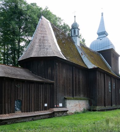 Zdjęcie nr 46: Drewniany kościół pw. św. Mikołaja w Polance jest budowlą orientowaną. Do prostokątnej nawy przylega węższe, wydłużone, trójbocznie zamknięte prezbiterium z piętrową zakrystią na osi o poligonalnym zamknięciu. Do zakrystii przylega od południa kruchta. Fragment północnej ściany prezbiterium jest murowany. Od zachodu do nawy dobudowano czworoboczną wieżę poprzedzoną przedsionkiem, który również dostawiono do nawy od południa. Prezbiterium i nawę wzniesiono na zrąb, natomiast wieżę w konstrukcji słupowej. Wieża na rzucie kwadratu posiada dwie kondygnacje. Dolna jest tej samej szerokości co nawa, górna natomiast znacznie węższa. Jej masyw podzielono smukłymi pilastrami i lizenami, zaś poniżej profilowanego gzymsu koronującego umieszczono wyrzynaną w desce koronkę. Kondygnacje oddzielono daszkiem gontowym zlewającym się po bokach z dachem kościoła. Wieżę nakryto kopulastym hełmem blaszanym, zwieńczonym blaszanym obeliskiem z krzyżem. Prezbiterium i nawę nakryto eternitowym dachem siodłowym podkreślonym profilowanym gzymsem. Nad nawą w części wschodniej zainstalowano wieżyczkę na sygnaturkę w formie wielobocznego graniastosłupa przykrytego cebulastą banią z krzyżem. Dokoła kościoła założono daszek gontowy chroniący podwaliny. Pod kościołem urządzono kryptę grzebalną. Wnętrze kościoła artykułowano za pomocą pilastrów i gzymsu. Całość nakryto stropem z fasetą. Otwór tęczowy uzyskał kształt trójlistnego, ściętego łuku, wspartego na filarkach ustawionych na profilowanej belce zawieszonej na kroksztynach. W części zachodniej nawy urządzono chór muzyczny, wsparty na dwóch kolumnach jońskich z przedpiersiem rozczłonkowanym balasami. We wnętrzu ustawiono ołtarz główny i dwa ołtarze boczne oraz ambonę, a na chórze muzycznym zainstalowano prospekt organowy.
