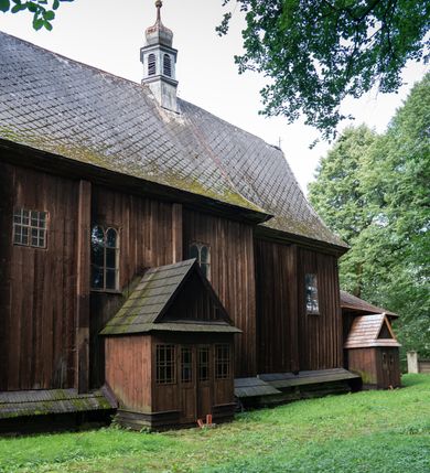Zdjęcie nr 48: Drewniany kościół pw. św. Mikołaja w Polance jest budowlą orientowaną. Do prostokątnej nawy przylega węższe, wydłużone, trójbocznie zamknięte prezbiterium z piętrową zakrystią na osi o poligonalnym zamknięciu. Do zakrystii przylega od południa kruchta. Fragment północnej ściany prezbiterium jest murowany. Od zachodu do nawy dobudowano czworoboczną wieżę poprzedzoną przedsionkiem, który również dostawiono do nawy od południa. Prezbiterium i nawę wzniesiono na zrąb, natomiast wieżę w konstrukcji słupowej. Wieża na rzucie kwadratu posiada dwie kondygnacje. Dolna jest tej samej szerokości co nawa, górna natomiast znacznie węższa. Jej masyw podzielono smukłymi pilastrami i lizenami, zaś poniżej profilowanego gzymsu koronującego umieszczono wyrzynaną w desce koronkę. Kondygnacje oddzielono daszkiem gontowym zlewającym się po bokach z dachem kościoła. Wieżę nakryto kopulastym hełmem blaszanym, zwieńczonym blaszanym obeliskiem z krzyżem. Prezbiterium i nawę nakryto eternitowym dachem siodłowym podkreślonym profilowanym gzymsem. Nad nawą w części wschodniej zainstalowano wieżyczkę na sygnaturkę w formie wielobocznego graniastosłupa przykrytego cebulastą banią z krzyżem. Dokoła kościoła założono daszek gontowy chroniący podwaliny. Pod kościołem urządzono kryptę grzebalną. Wnętrze kościoła artykułowano za pomocą pilastrów i gzymsu. Całość nakryto stropem z fasetą. Otwór tęczowy uzyskał kształt trójlistnego, ściętego łuku, wspartego na filarkach ustawionych na profilowanej belce zawieszonej na kroksztynach. W części zachodniej nawy urządzono chór muzyczny, wsparty na dwóch kolumnach jońskich z przedpiersiem rozczłonkowanym balasami. We wnętrzu ustawiono ołtarz główny i dwa ołtarze boczne oraz ambonę, a na chórze muzycznym zainstalowano prospekt organowy.