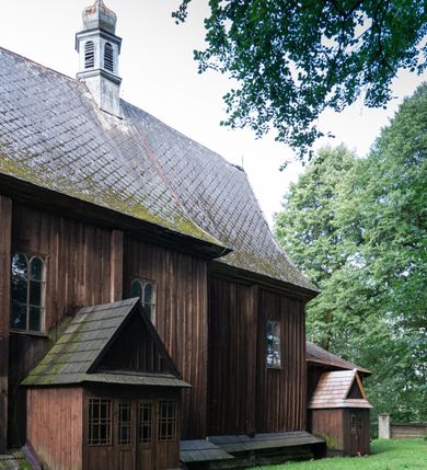 Zdjęcie nr 27: Drewniany kościół pw. św. Mikołaja w Polance jest budowlą orientowaną. Do prostokątnej nawy przylega węższe, wydłużone, trójbocznie zamknięte prezbiterium z piętrową zakrystią na osi o poligonalnym zamknięciu. Do zakrystii przylega od południa kruchta. Fragment północnej ściany prezbiterium jest murowany. Od zachodu do nawy dobudowano czworoboczną wieżę poprzedzoną przedsionkiem, który również dostawiono do nawy od południa. Prezbiterium i nawę wzniesiono na zrąb, natomiast wieżę w konstrukcji słupowej. Wieża na rzucie kwadratu posiada dwie kondygnacje. Dolna jest tej samej szerokości co nawa, górna natomiast znacznie węższa. Jej masyw podzielono smukłymi pilastrami i lizenami, zaś poniżej profilowanego gzymsu koronującego umieszczono wyrzynaną w desce koronkę. Kondygnacje oddzielono daszkiem gontowym zlewającym się po bokach z dachem kościoła. Wieżę nakryto kopulastym hełmem blaszanym, zwieńczonym blaszanym obeliskiem z krzyżem. Prezbiterium i nawę nakryto eternitowym dachem siodłowym podkreślonym profilowanym gzymsem. Nad nawą w części wschodniej zainstalowano wieżyczkę na sygnaturkę w formie wielobocznego graniastosłupa przykrytego cebulastą banią z krzyżem. Dokoła kościoła założono daszek gontowy chroniący podwaliny. Pod kościołem urządzono kryptę grzebalną. Wnętrze kościoła artykułowano za pomocą pilastrów i gzymsu. Całość nakryto stropem z fasetą. Otwór tęczowy uzyskał kształt trójlistnego, ściętego łuku, wspartego na filarkach ustawionych na profilowanej belce zawieszonej na kroksztynach. W części zachodniej nawy urządzono chór muzyczny, wsparty na dwóch kolumnach jońskich z przedpiersiem rozczłonkowanym balasami. We wnętrzu ustawiono ołtarz główny i dwa ołtarze boczne oraz ambonę, a na chórze muzycznym zainstalowano prospekt organowy.