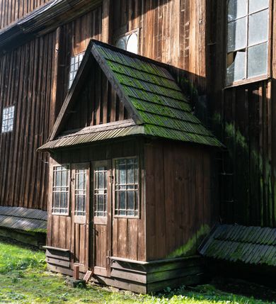 Zdjęcie nr 26: Drewniany kościół pw. św. Mikołaja w Polance jest budowlą orientowaną. Do prostokątnej nawy przylega węższe, wydłużone, trójbocznie zamknięte prezbiterium z piętrową zakrystią na osi o poligonalnym zamknięciu. Do zakrystii przylega od południa kruchta. Fragment północnej ściany prezbiterium jest murowany. Od zachodu do nawy dobudowano czworoboczną wieżę poprzedzoną przedsionkiem, który również dostawiono do nawy od południa. Prezbiterium i nawę wzniesiono na zrąb, natomiast wieżę w konstrukcji słupowej. Wieża na rzucie kwadratu posiada dwie kondygnacje. Dolna jest tej samej szerokości co nawa, górna natomiast znacznie węższa. Jej masyw podzielono smukłymi pilastrami i lizenami, zaś poniżej profilowanego gzymsu koronującego umieszczono wyrzynaną w desce koronkę. Kondygnacje oddzielono daszkiem gontowym zlewającym się po bokach z dachem kościoła. Wieżę nakryto kopulastym hełmem blaszanym, zwieńczonym blaszanym obeliskiem z krzyżem. Prezbiterium i nawę nakryto eternitowym dachem siodłowym podkreślonym profilowanym gzymsem. Nad nawą w części wschodniej zainstalowano wieżyczkę na sygnaturkę w formie wielobocznego graniastosłupa przykrytego cebulastą banią z krzyżem. Dokoła kościoła założono daszek gontowy chroniący podwaliny. Pod kościołem urządzono kryptę grzebalną. Wnętrze kościoła artykułowano za pomocą pilastrów i gzymsu. Całość nakryto stropem z fasetą. Otwór tęczowy uzyskał kształt trójlistnego, ściętego łuku, wspartego na filarkach ustawionych na profilowanej belce zawieszonej na kroksztynach. W części zachodniej nawy urządzono chór muzyczny, wsparty na dwóch kolumnach jońskich z przedpiersiem rozczłonkowanym balasami. We wnętrzu ustawiono ołtarz główny i dwa ołtarze boczne oraz ambonę, a na chórze muzycznym zainstalowano prospekt organowy.