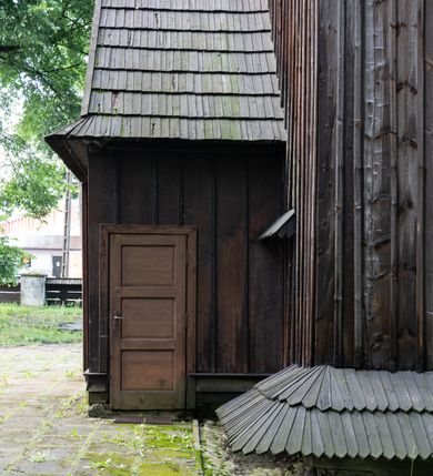 Zdjęcie nr 56: Drewniany kościół pw. św. Mikołaja w Polance jest budowlą orientowaną. Do prostokątnej nawy przylega węższe, wydłużone, trójbocznie zamknięte prezbiterium z piętrową zakrystią na osi o poligonalnym zamknięciu. Do zakrystii przylega od południa kruchta. Fragment północnej ściany prezbiterium jest murowany. Od zachodu do nawy dobudowano czworoboczną wieżę poprzedzoną przedsionkiem, który również dostawiono do nawy od południa. Prezbiterium i nawę wzniesiono na zrąb, natomiast wieżę w konstrukcji słupowej. Wieża na rzucie kwadratu posiada dwie kondygnacje. Dolna jest tej samej szerokości co nawa, górna natomiast znacznie węższa. Jej masyw podzielono smukłymi pilastrami i lizenami, zaś poniżej profilowanego gzymsu koronującego umieszczono wyrzynaną w desce koronkę. Kondygnacje oddzielono daszkiem gontowym zlewającym się po bokach z dachem kościoła. Wieżę nakryto kopulastym hełmem blaszanym, zwieńczonym blaszanym obeliskiem z krzyżem. Prezbiterium i nawę nakryto eternitowym dachem siodłowym podkreślonym profilowanym gzymsem. Nad nawą w części wschodniej zainstalowano wieżyczkę na sygnaturkę w formie wielobocznego graniastosłupa przykrytego cebulastą banią z krzyżem. Dokoła kościoła założono daszek gontowy chroniący podwaliny. Pod kościołem urządzono kryptę grzebalną. Wnętrze kościoła artykułowano za pomocą pilastrów i gzymsu. Całość nakryto stropem z fasetą. Otwór tęczowy uzyskał kształt trójlistnego, ściętego łuku, wspartego na filarkach ustawionych na profilowanej belce zawieszonej na kroksztynach. W części zachodniej nawy urządzono chór muzyczny, wsparty na dwóch kolumnach jońskich z przedpiersiem rozczłonkowanym balasami. We wnętrzu ustawiono ołtarz główny i dwa ołtarze boczne oraz ambonę, a na chórze muzycznym zainstalowano prospekt organowy.