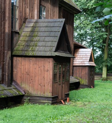 Zdjęcie nr 32: Drewniany kościół pw. św. Mikołaja w Polance jest budowlą orientowaną. Do prostokątnej nawy przylega węższe, wydłużone, trójbocznie zamknięte prezbiterium z piętrową zakrystią na osi o poligonalnym zamknięciu. Do zakrystii przylega od południa kruchta. Fragment północnej ściany prezbiterium jest murowany. Od zachodu do nawy dobudowano czworoboczną wieżę poprzedzoną przedsionkiem, który również dostawiono do nawy od południa. Prezbiterium i nawę wzniesiono na zrąb, natomiast wieżę w konstrukcji słupowej. Wieża na rzucie kwadratu posiada dwie kondygnacje. Dolna jest tej samej szerokości co nawa, górna natomiast znacznie węższa. Jej masyw podzielono smukłymi pilastrami i lizenami, zaś poniżej profilowanego gzymsu koronującego umieszczono wyrzynaną w desce koronkę. Kondygnacje oddzielono daszkiem gontowym zlewającym się po bokach z dachem kościoła. Wieżę nakryto kopulastym hełmem blaszanym, zwieńczonym blaszanym obeliskiem z krzyżem. Prezbiterium i nawę nakryto eternitowym dachem siodłowym podkreślonym profilowanym gzymsem. Nad nawą w części wschodniej zainstalowano wieżyczkę na sygnaturkę w formie wielobocznego graniastosłupa przykrytego cebulastą banią z krzyżem. Dokoła kościoła założono daszek gontowy chroniący podwaliny. Pod kościołem urządzono kryptę grzebalną. Wnętrze kościoła artykułowano za pomocą pilastrów i gzymsu. Całość nakryto stropem z fasetą. Otwór tęczowy uzyskał kształt trójlistnego, ściętego łuku, wspartego na filarkach ustawionych na profilowanej belce zawieszonej na kroksztynach. W części zachodniej nawy urządzono chór muzyczny, wsparty na dwóch kolumnach jońskich z przedpiersiem rozczłonkowanym balasami. We wnętrzu ustawiono ołtarz główny i dwa ołtarze boczne oraz ambonę, a na chórze muzycznym zainstalowano prospekt organowy.