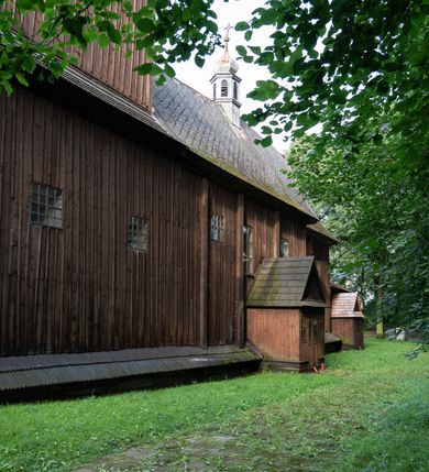 Zdjęcie nr 31: Drewniany kościół pw. św. Mikołaja w Polance jest budowlą orientowaną. Do prostokątnej nawy przylega węższe, wydłużone, trójbocznie zamknięte prezbiterium z piętrową zakrystią na osi o poligonalnym zamknięciu. Do zakrystii przylega od południa kruchta. Fragment północnej ściany prezbiterium jest murowany. Od zachodu do nawy dobudowano czworoboczną wieżę poprzedzoną przedsionkiem, który również dostawiono do nawy od południa. Prezbiterium i nawę wzniesiono na zrąb, natomiast wieżę w konstrukcji słupowej. Wieża na rzucie kwadratu posiada dwie kondygnacje. Dolna jest tej samej szerokości co nawa, górna natomiast znacznie węższa. Jej masyw podzielono smukłymi pilastrami i lizenami, zaś poniżej profilowanego gzymsu koronującego umieszczono wyrzynaną w desce koronkę. Kondygnacje oddzielono daszkiem gontowym zlewającym się po bokach z dachem kościoła. Wieżę nakryto kopulastym hełmem blaszanym, zwieńczonym blaszanym obeliskiem z krzyżem. Prezbiterium i nawę nakryto eternitowym dachem siodłowym podkreślonym profilowanym gzymsem. Nad nawą w części wschodniej zainstalowano wieżyczkę na sygnaturkę w formie wielobocznego graniastosłupa przykrytego cebulastą banią z krzyżem. Dokoła kościoła założono daszek gontowy chroniący podwaliny. Pod kościołem urządzono kryptę grzebalną. Wnętrze kościoła artykułowano za pomocą pilastrów i gzymsu. Całość nakryto stropem z fasetą. Otwór tęczowy uzyskał kształt trójlistnego, ściętego łuku, wspartego na filarkach ustawionych na profilowanej belce zawieszonej na kroksztynach. W części zachodniej nawy urządzono chór muzyczny, wsparty na dwóch kolumnach jońskich z przedpiersiem rozczłonkowanym balasami. We wnętrzu ustawiono ołtarz główny i dwa ołtarze boczne oraz ambonę, a na chórze muzycznym zainstalowano prospekt organowy.