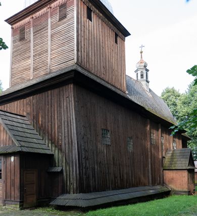 Zdjęcie nr 33: Drewniany kościół pw. św. Mikołaja w Polance jest budowlą orientowaną. Do prostokątnej nawy przylega węższe, wydłużone, trójbocznie zamknięte prezbiterium z piętrową zakrystią na osi o poligonalnym zamknięciu. Do zakrystii przylega od południa kruchta. Fragment północnej ściany prezbiterium jest murowany. Od zachodu do nawy dobudowano czworoboczną wieżę poprzedzoną przedsionkiem, który również dostawiono do nawy od południa. Prezbiterium i nawę wzniesiono na zrąb, natomiast wieżę w konstrukcji słupowej. Wieża na rzucie kwadratu posiada dwie kondygnacje. Dolna jest tej samej szerokości co nawa, górna natomiast znacznie węższa. Jej masyw podzielono smukłymi pilastrami i lizenami, zaś poniżej profilowanego gzymsu koronującego umieszczono wyrzynaną w desce koronkę. Kondygnacje oddzielono daszkiem gontowym zlewającym się po bokach z dachem kościoła. Wieżę nakryto kopulastym hełmem blaszanym, zwieńczonym blaszanym obeliskiem z krzyżem. Prezbiterium i nawę nakryto eternitowym dachem siodłowym podkreślonym profilowanym gzymsem. Nad nawą w części wschodniej zainstalowano wieżyczkę na sygnaturkę w formie wielobocznego graniastosłupa przykrytego cebulastą banią z krzyżem. Dokoła kościoła założono daszek gontowy chroniący podwaliny. Pod kościołem urządzono kryptę grzebalną. Wnętrze kościoła artykułowano za pomocą pilastrów i gzymsu. Całość nakryto stropem z fasetą. Otwór tęczowy uzyskał kształt trójlistnego, ściętego łuku, wspartego na filarkach ustawionych na profilowanej belce zawieszonej na kroksztynach. W części zachodniej nawy urządzono chór muzyczny, wsparty na dwóch kolumnach jońskich z przedpiersiem rozczłonkowanym balasami. We wnętrzu ustawiono ołtarz główny i dwa ołtarze boczne oraz ambonę, a na chórze muzycznym zainstalowano prospekt organowy.