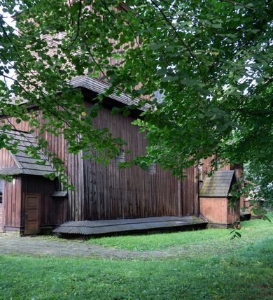 Zdjęcie nr 34: Drewniany kościół pw. św. Mikołaja w Polance jest budowlą orientowaną. Do prostokątnej nawy przylega węższe, wydłużone, trójbocznie zamknięte prezbiterium z piętrową zakrystią na osi o poligonalnym zamknięciu. Do zakrystii przylega od południa kruchta. Fragment północnej ściany prezbiterium jest murowany. Od zachodu do nawy dobudowano czworoboczną wieżę poprzedzoną przedsionkiem, który również dostawiono do nawy od południa. Prezbiterium i nawę wzniesiono na zrąb, natomiast wieżę w konstrukcji słupowej. Wieża na rzucie kwadratu posiada dwie kondygnacje. Dolna jest tej samej szerokości co nawa, górna natomiast znacznie węższa. Jej masyw podzielono smukłymi pilastrami i lizenami, zaś poniżej profilowanego gzymsu koronującego umieszczono wyrzynaną w desce koronkę. Kondygnacje oddzielono daszkiem gontowym zlewającym się po bokach z dachem kościoła. Wieżę nakryto kopulastym hełmem blaszanym, zwieńczonym blaszanym obeliskiem z krzyżem. Prezbiterium i nawę nakryto eternitowym dachem siodłowym podkreślonym profilowanym gzymsem. Nad nawą w części wschodniej zainstalowano wieżyczkę na sygnaturkę w formie wielobocznego graniastosłupa przykrytego cebulastą banią z krzyżem. Dokoła kościoła założono daszek gontowy chroniący podwaliny. Pod kościołem urządzono kryptę grzebalną. Wnętrze kościoła artykułowano za pomocą pilastrów i gzymsu. Całość nakryto stropem z fasetą. Otwór tęczowy uzyskał kształt trójlistnego, ściętego łuku, wspartego na filarkach ustawionych na profilowanej belce zawieszonej na kroksztynach. W części zachodniej nawy urządzono chór muzyczny, wsparty na dwóch kolumnach jońskich z przedpiersiem rozczłonkowanym balasami. We wnętrzu ustawiono ołtarz główny i dwa ołtarze boczne oraz ambonę, a na chórze muzycznym zainstalowano prospekt organowy.