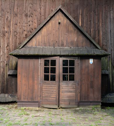 Zdjęcie nr 51: Drewniany kościół pw. św. Mikołaja w Polance jest budowlą orientowaną. Do prostokątnej nawy przylega węższe, wydłużone, trójbocznie zamknięte prezbiterium z piętrową zakrystią na osi o poligonalnym zamknięciu. Do zakrystii przylega od południa kruchta. Fragment północnej ściany prezbiterium jest murowany. Od zachodu do nawy dobudowano czworoboczną wieżę poprzedzoną przedsionkiem, który również dostawiono do nawy od południa. Prezbiterium i nawę wzniesiono na zrąb, natomiast wieżę w konstrukcji słupowej. Wieża na rzucie kwadratu posiada dwie kondygnacje. Dolna jest tej samej szerokości co nawa, górna natomiast znacznie węższa. Jej masyw podzielono smukłymi pilastrami i lizenami, zaś poniżej profilowanego gzymsu koronującego umieszczono wyrzynaną w desce koronkę. Kondygnacje oddzielono daszkiem gontowym zlewającym się po bokach z dachem kościoła. Wieżę nakryto kopulastym hełmem blaszanym, zwieńczonym blaszanym obeliskiem z krzyżem. Prezbiterium i nawę nakryto eternitowym dachem siodłowym podkreślonym profilowanym gzymsem. Nad nawą w części wschodniej zainstalowano wieżyczkę na sygnaturkę w formie wielobocznego graniastosłupa przykrytego cebulastą banią z krzyżem. Dokoła kościoła założono daszek gontowy chroniący podwaliny. Pod kościołem urządzono kryptę grzebalną. Wnętrze kościoła artykułowano za pomocą pilastrów i gzymsu. Całość nakryto stropem z fasetą. Otwór tęczowy uzyskał kształt trójlistnego, ściętego łuku, wspartego na filarkach ustawionych na profilowanej belce zawieszonej na kroksztynach. W części zachodniej nawy urządzono chór muzyczny, wsparty na dwóch kolumnach jońskich z przedpiersiem rozczłonkowanym balasami. We wnętrzu ustawiono ołtarz główny i dwa ołtarze boczne oraz ambonę, a na chórze muzycznym zainstalowano prospekt organowy.