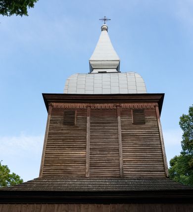 Zdjęcie nr 28: Drewniany kościół pw. św. Mikołaja w Polance jest budowlą orientowaną. Do prostokątnej nawy przylega węższe, wydłużone, trójbocznie zamknięte prezbiterium z piętrową zakrystią na osi o poligonalnym zamknięciu. Do zakrystii przylega od południa kruchta. Fragment północnej ściany prezbiterium jest murowany. Od zachodu do nawy dobudowano czworoboczną wieżę poprzedzoną przedsionkiem, który również dostawiono do nawy od południa. Prezbiterium i nawę wzniesiono na zrąb, natomiast wieżę w konstrukcji słupowej. Wieża na rzucie kwadratu posiada dwie kondygnacje. Dolna jest tej samej szerokości co nawa, górna natomiast znacznie węższa. Jej masyw podzielono smukłymi pilastrami i lizenami, zaś poniżej profilowanego gzymsu koronującego umieszczono wyrzynaną w desce koronkę. Kondygnacje oddzielono daszkiem gontowym zlewającym się po bokach z dachem kościoła. Wieżę nakryto kopulastym hełmem blaszanym, zwieńczonym blaszanym obeliskiem z krzyżem. Prezbiterium i nawę nakryto eternitowym dachem siodłowym podkreślonym profilowanym gzymsem. Nad nawą w części wschodniej zainstalowano wieżyczkę na sygnaturkę w formie wielobocznego graniastosłupa przykrytego cebulastą banią z krzyżem. Dokoła kościoła założono daszek gontowy chroniący podwaliny. Pod kościołem urządzono kryptę grzebalną. Wnętrze kościoła artykułowano za pomocą pilastrów i gzymsu. Całość nakryto stropem z fasetą. Otwór tęczowy uzyskał kształt trójlistnego, ściętego łuku, wspartego na filarkach ustawionych na profilowanej belce zawieszonej na kroksztynach. W części zachodniej nawy urządzono chór muzyczny, wsparty na dwóch kolumnach jońskich z przedpiersiem rozczłonkowanym balasami. We wnętrzu ustawiono ołtarz główny i dwa ołtarze boczne oraz ambonę, a na chórze muzycznym zainstalowano prospekt organowy.