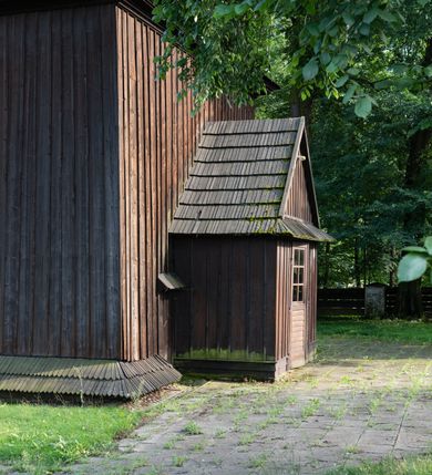 Zdjęcie nr 59: Drewniany kościół pw. św. Mikołaja w Polance jest budowlą orientowaną. Do prostokątnej nawy przylega węższe, wydłużone, trójbocznie zamknięte prezbiterium z piętrową zakrystią na osi o poligonalnym zamknięciu. Do zakrystii przylega od południa kruchta. Fragment północnej ściany prezbiterium jest murowany. Od zachodu do nawy dobudowano czworoboczną wieżę poprzedzoną przedsionkiem, który również dostawiono do nawy od południa. Prezbiterium i nawę wzniesiono na zrąb, natomiast wieżę w konstrukcji słupowej. Wieża na rzucie kwadratu posiada dwie kondygnacje. Dolna jest tej samej szerokości co nawa, górna natomiast znacznie węższa. Jej masyw podzielono smukłymi pilastrami i lizenami, zaś poniżej profilowanego gzymsu koronującego umieszczono wyrzynaną w desce koronkę. Kondygnacje oddzielono daszkiem gontowym zlewającym się po bokach z dachem kościoła. Wieżę nakryto kopulastym hełmem blaszanym, zwieńczonym blaszanym obeliskiem z krzyżem. Prezbiterium i nawę nakryto eternitowym dachem siodłowym podkreślonym profilowanym gzymsem. Nad nawą w części wschodniej zainstalowano wieżyczkę na sygnaturkę w formie wielobocznego graniastosłupa przykrytego cebulastą banią z krzyżem. Dokoła kościoła założono daszek gontowy chroniący podwaliny. Pod kościołem urządzono kryptę grzebalną. Wnętrze kościoła artykułowano za pomocą pilastrów i gzymsu. Całość nakryto stropem z fasetą. Otwór tęczowy uzyskał kształt trójlistnego, ściętego łuku, wspartego na filarkach ustawionych na profilowanej belce zawieszonej na kroksztynach. W części zachodniej nawy urządzono chór muzyczny, wsparty na dwóch kolumnach jońskich z przedpiersiem rozczłonkowanym balasami. We wnętrzu ustawiono ołtarz główny i dwa ołtarze boczne oraz ambonę, a na chórze muzycznym zainstalowano prospekt organowy.