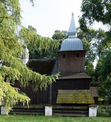 Zdjęcie nr 45: Drewniany kościół pw. św. Mikołaja w Polance jest budowlą orientowaną. Do prostokątnej nawy przylega węższe, wydłużone, trójbocznie zamknięte prezbiterium z piętrową zakrystią na osi o poligonalnym zamknięciu. Do zakrystii przylega od południa kruchta. Fragment północnej ściany prezbiterium jest murowany. Od zachodu do nawy dobudowano czworoboczną wieżę poprzedzoną przedsionkiem, który również dostawiono do nawy od południa. Prezbiterium i nawę wzniesiono na zrąb, natomiast wieżę w konstrukcji słupowej. Wieża na rzucie kwadratu posiada dwie kondygnacje. Dolna jest tej samej szerokości co nawa, górna natomiast znacznie węższa. Jej masyw podzielono smukłymi pilastrami i lizenami, zaś poniżej profilowanego gzymsu koronującego umieszczono wyrzynaną w desce koronkę. Kondygnacje oddzielono daszkiem gontowym zlewającym się po bokach z dachem kościoła. Wieżę nakryto kopulastym hełmem blaszanym, zwieńczonym blaszanym obeliskiem z krzyżem. Prezbiterium i nawę nakryto eternitowym dachem siodłowym podkreślonym profilowanym gzymsem. Nad nawą w części wschodniej zainstalowano wieżyczkę na sygnaturkę w formie wielobocznego graniastosłupa przykrytego cebulastą banią z krzyżem. Dokoła kościoła założono daszek gontowy chroniący podwaliny. Pod kościołem urządzono kryptę grzebalną. Wnętrze kościoła artykułowano za pomocą pilastrów i gzymsu. Całość nakryto stropem z fasetą. Otwór tęczowy uzyskał kształt trójlistnego, ściętego łuku, wspartego na filarkach ustawionych na profilowanej belce zawieszonej na kroksztynach. W części zachodniej nawy urządzono chór muzyczny, wsparty na dwóch kolumnach jońskich z przedpiersiem rozczłonkowanym balasami. We wnętrzu ustawiono ołtarz główny i dwa ołtarze boczne oraz ambonę, a na chórze muzycznym zainstalowano prospekt organowy.
