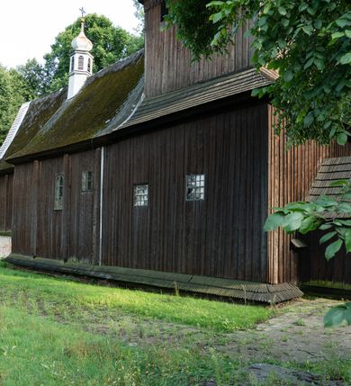 Zdjęcie nr 24: Drewniany kościół pw. św. Mikołaja w Polance jest budowlą orientowaną. Do prostokątnej nawy przylega węższe, wydłużone, trójbocznie zamknięte prezbiterium z piętrową zakrystią na osi o poligonalnym zamknięciu. Do zakrystii przylega od południa kruchta. Fragment północnej ściany prezbiterium jest murowany. Od zachodu do nawy dobudowano czworoboczną wieżę poprzedzoną przedsionkiem, który również dostawiono do nawy od południa. Prezbiterium i nawę wzniesiono na zrąb, natomiast wieżę w konstrukcji słupowej. Wieża na rzucie kwadratu posiada dwie kondygnacje. Dolna jest tej samej szerokości co nawa, górna natomiast znacznie węższa. Jej masyw podzielono smukłymi pilastrami i lizenami, zaś poniżej profilowanego gzymsu koronującego umieszczono wyrzynaną w desce koronkę. Kondygnacje oddzielono daszkiem gontowym zlewającym się po bokach z dachem kościoła. Wieżę nakryto kopulastym hełmem blaszanym, zwieńczonym blaszanym obeliskiem z krzyżem. Prezbiterium i nawę nakryto eternitowym dachem siodłowym podkreślonym profilowanym gzymsem. Nad nawą w części wschodniej zainstalowano wieżyczkę na sygnaturkę w formie wielobocznego graniastosłupa przykrytego cebulastą banią z krzyżem. Dokoła kościoła założono daszek gontowy chroniący podwaliny. Pod kościołem urządzono kryptę grzebalną. Wnętrze kościoła artykułowano za pomocą pilastrów i gzymsu. Całość nakryto stropem z fasetą. Otwór tęczowy uzyskał kształt trójlistnego, ściętego łuku, wspartego na filarkach ustawionych na profilowanej belce zawieszonej na kroksztynach. W części zachodniej nawy urządzono chór muzyczny, wsparty na dwóch kolumnach jońskich z przedpiersiem rozczłonkowanym balasami. We wnętrzu ustawiono ołtarz główny i dwa ołtarze boczne oraz ambonę, a na chórze muzycznym zainstalowano prospekt organowy.