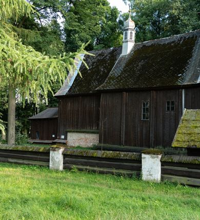 Zdjęcie nr 63: Drewniany kościół pw. św. Mikołaja w Polance jest budowlą orientowaną. Do prostokątnej nawy przylega węższe, wydłużone, trójbocznie zamknięte prezbiterium z piętrową zakrystią na osi o poligonalnym zamknięciu. Do zakrystii przylega od południa kruchta. Fragment północnej ściany prezbiterium jest murowany. Od zachodu do nawy dobudowano czworoboczną wieżę poprzedzoną przedsionkiem, który również dostawiono do nawy od południa. Prezbiterium i nawę wzniesiono na zrąb, natomiast wieżę w konstrukcji słupowej. Wieża na rzucie kwadratu posiada dwie kondygnacje. Dolna jest tej samej szerokości co nawa, górna natomiast znacznie węższa. Jej masyw podzielono smukłymi pilastrami i lizenami, zaś poniżej profilowanego gzymsu koronującego umieszczono wyrzynaną w desce koronkę. Kondygnacje oddzielono daszkiem gontowym zlewającym się po bokach z dachem kościoła. Wieżę nakryto kopulastym hełmem blaszanym, zwieńczonym blaszanym obeliskiem z krzyżem. Prezbiterium i nawę nakryto eternitowym dachem siodłowym podkreślonym profilowanym gzymsem. Nad nawą w części wschodniej zainstalowano wieżyczkę na sygnaturkę w formie wielobocznego graniastosłupa przykrytego cebulastą banią z krzyżem. Dokoła kościoła założono daszek gontowy chroniący podwaliny. Pod kościołem urządzono kryptę grzebalną. Wnętrze kościoła artykułowano za pomocą pilastrów i gzymsu. Całość nakryto stropem z fasetą. Otwór tęczowy uzyskał kształt trójlistnego, ściętego łuku, wspartego na filarkach ustawionych na profilowanej belce zawieszonej na kroksztynach. W części zachodniej nawy urządzono chór muzyczny, wsparty na dwóch kolumnach jońskich z przedpiersiem rozczłonkowanym balasami. We wnętrzu ustawiono ołtarz główny i dwa ołtarze boczne oraz ambonę, a na chórze muzycznym zainstalowano prospekt organowy.