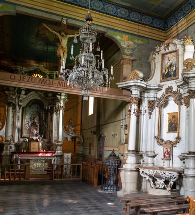 Zdjęcie nr 4: Drewniany kościół pw. św. Mikołaja w Polance jest budowlą orientowaną. Do prostokątnej nawy przylega węższe, wydłużone, trójbocznie zamknięte prezbiterium z piętrową zakrystią na osi o poligonalnym zamknięciu. Do zakrystii przylega od południa kruchta. Fragment północnej ściany prezbiterium jest murowany. Od zachodu do nawy dobudowano czworoboczną wieżę poprzedzoną przedsionkiem, który również dostawiono do nawy od południa. Prezbiterium i nawę wzniesiono na zrąb, natomiast wieżę w konstrukcji słupowej. Wieża na rzucie kwadratu posiada dwie kondygnacje. Dolna jest tej samej szerokości co nawa, górna natomiast znacznie węższa. Jej masyw podzielono smukłymi pilastrami i lizenami, zaś poniżej profilowanego gzymsu koronującego umieszczono wyrzynaną w desce koronkę. Kondygnacje oddzielono daszkiem gontowym zlewającym się po bokach z dachem kościoła. Wieżę nakryto kopulastym hełmem blaszanym, zwieńczonym blaszanym obeliskiem z krzyżem. Prezbiterium i nawę nakryto eternitowym dachem siodłowym podkreślonym profilowanym gzymsem. Nad nawą w części wschodniej zainstalowano wieżyczkę na sygnaturkę w formie wielobocznego graniastosłupa przykrytego cebulastą banią z krzyżem. Dokoła kościoła założono daszek gontowy chroniący podwaliny. Pod kościołem urządzono kryptę grzebalną. Wnętrze kościoła artykułowano za pomocą pilastrów i gzymsu. Całość nakryto stropem z fasetą. Otwór tęczowy uzyskał kształt trójlistnego, ściętego łuku, wspartego na filarkach ustawionych na profilowanej belce zawieszonej na kroksztynach. W części zachodniej nawy urządzono chór muzyczny, wsparty na dwóch kolumnach jońskich z przedpiersiem rozczłonkowanym balasami. We wnętrzu ustawiono ołtarz główny i dwa ołtarze boczne oraz ambonę, a na chórze muzycznym zainstalowano prospekt organowy.