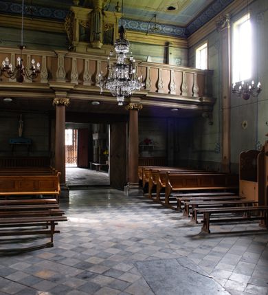 Zdjęcie nr 15: Drewniany kościół pw. św. Mikołaja w Polance jest budowlą orientowaną. Do prostokątnej nawy przylega węższe, wydłużone, trójbocznie zamknięte prezbiterium z piętrową zakrystią na osi o poligonalnym zamknięciu. Do zakrystii przylega od południa kruchta. Fragment północnej ściany prezbiterium jest murowany. Od zachodu do nawy dobudowano czworoboczną wieżę poprzedzoną przedsionkiem, który również dostawiono do nawy od południa. Prezbiterium i nawę wzniesiono na zrąb, natomiast wieżę w konstrukcji słupowej. Wieża na rzucie kwadratu posiada dwie kondygnacje. Dolna jest tej samej szerokości co nawa, górna natomiast znacznie węższa. Jej masyw podzielono smukłymi pilastrami i lizenami, zaś poniżej profilowanego gzymsu koronującego umieszczono wyrzynaną w desce koronkę. Kondygnacje oddzielono daszkiem gontowym zlewającym się po bokach z dachem kościoła. Wieżę nakryto kopulastym hełmem blaszanym, zwieńczonym blaszanym obeliskiem z krzyżem. Prezbiterium i nawę nakryto eternitowym dachem siodłowym podkreślonym profilowanym gzymsem. Nad nawą w części wschodniej zainstalowano wieżyczkę na sygnaturkę w formie wielobocznego graniastosłupa przykrytego cebulastą banią z krzyżem. Dokoła kościoła założono daszek gontowy chroniący podwaliny. Pod kościołem urządzono kryptę grzebalną. Wnętrze kościoła artykułowano za pomocą pilastrów i gzymsu. Całość nakryto stropem z fasetą. Otwór tęczowy uzyskał kształt trójlistnego, ściętego łuku, wspartego na filarkach ustawionych na profilowanej belce zawieszonej na kroksztynach. W części zachodniej nawy urządzono chór muzyczny, wsparty na dwóch kolumnach jońskich z przedpiersiem rozczłonkowanym balasami. We wnętrzu ustawiono ołtarz główny i dwa ołtarze boczne oraz ambonę, a na chórze muzycznym zainstalowano prospekt organowy.