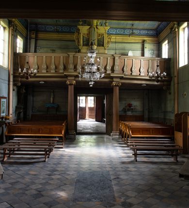 Zdjęcie nr 13: Drewniany kościół pw. św. Mikołaja w Polance jest budowlą orientowaną. Do prostokątnej nawy przylega węższe, wydłużone, trójbocznie zamknięte prezbiterium z piętrową zakrystią na osi o poligonalnym zamknięciu. Do zakrystii przylega od południa kruchta. Fragment północnej ściany prezbiterium jest murowany. Od zachodu do nawy dobudowano czworoboczną wieżę poprzedzoną przedsionkiem, który również dostawiono do nawy od południa. Prezbiterium i nawę wzniesiono na zrąb, natomiast wieżę w konstrukcji słupowej. Wieża na rzucie kwadratu posiada dwie kondygnacje. Dolna jest tej samej szerokości co nawa, górna natomiast znacznie węższa. Jej masyw podzielono smukłymi pilastrami i lizenami, zaś poniżej profilowanego gzymsu koronującego umieszczono wyrzynaną w desce koronkę. Kondygnacje oddzielono daszkiem gontowym zlewającym się po bokach z dachem kościoła. Wieżę nakryto kopulastym hełmem blaszanym, zwieńczonym blaszanym obeliskiem z krzyżem. Prezbiterium i nawę nakryto eternitowym dachem siodłowym podkreślonym profilowanym gzymsem. Nad nawą w części wschodniej zainstalowano wieżyczkę na sygnaturkę w formie wielobocznego graniastosłupa przykrytego cebulastą banią z krzyżem. Dokoła kościoła założono daszek gontowy chroniący podwaliny. Pod kościołem urządzono kryptę grzebalną. Wnętrze kościoła artykułowano za pomocą pilastrów i gzymsu. Całość nakryto stropem z fasetą. Otwór tęczowy uzyskał kształt trójlistnego, ściętego łuku, wspartego na filarkach ustawionych na profilowanej belce zawieszonej na kroksztynach. W części zachodniej nawy urządzono chór muzyczny, wsparty na dwóch kolumnach jońskich z przedpiersiem rozczłonkowanym balasami. We wnętrzu ustawiono ołtarz główny i dwa ołtarze boczne oraz ambonę, a na chórze muzycznym zainstalowano prospekt organowy.