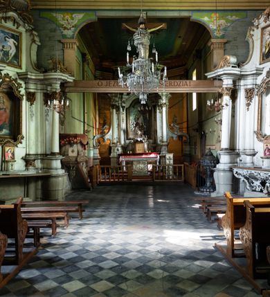 Zdjęcie nr 2: Drewniany kościół pw. św. Mikołaja w Polance jest budowlą orientowaną. Do prostokątnej nawy przylega węższe, wydłużone, trójbocznie zamknięte prezbiterium z piętrową zakrystią na osi o poligonalnym zamknięciu. Do zakrystii przylega od południa kruchta. Fragment północnej ściany prezbiterium jest murowany. Od zachodu do nawy dobudowano czworoboczną wieżę poprzedzoną przedsionkiem, który również dostawiono do nawy od południa. Prezbiterium i nawę wzniesiono na zrąb, natomiast wieżę w konstrukcji słupowej. Wieża na rzucie kwadratu posiada dwie kondygnacje. Dolna jest tej samej szerokości co nawa, górna natomiast znacznie węższa. Jej masyw podzielono smukłymi pilastrami i lizenami, zaś poniżej profilowanego gzymsu koronującego umieszczono wyrzynaną w desce koronkę. Kondygnacje oddzielono daszkiem gontowym zlewającym się po bokach z dachem kościoła. Wieżę nakryto kopulastym hełmem blaszanym, zwieńczonym blaszanym obeliskiem z krzyżem. Prezbiterium i nawę nakryto eternitowym dachem siodłowym podkreślonym profilowanym gzymsem. Nad nawą w części wschodniej zainstalowano wieżyczkę na sygnaturkę w formie wielobocznego graniastosłupa przykrytego cebulastą banią z krzyżem. Dokoła kościoła założono daszek gontowy chroniący podwaliny. Pod kościołem urządzono kryptę grzebalną. Wnętrze kościoła artykułowano za pomocą pilastrów i gzymsu. Całość nakryto stropem z fasetą. Otwór tęczowy uzyskał kształt trójlistnego, ściętego łuku, wspartego na filarkach ustawionych na profilowanej belce zawieszonej na kroksztynach. W części zachodniej nawy urządzono chór muzyczny, wsparty na dwóch kolumnach jońskich z przedpiersiem rozczłonkowanym balasami. We wnętrzu ustawiono ołtarz główny i dwa ołtarze boczne oraz ambonę, a na chórze muzycznym zainstalowano prospekt organowy.