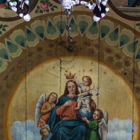 Zdjęcie nr 1: Polichromia malarska we wnętrzu drewnianego kościoła parafialnego w Polance Wielkiej zachowała się w prezbiterium, nawie oraz w przedsionku urządzonym w przyziemiu wieży. W prezbiterium i nawie zastosowano podział ramowy uwzględniający drewniane pilastry artykułujące ściany, gzyms oraz fasetę. Na ścianach pomiędzy pilastrami wprowadzono czworoboczne panneau o narożach utworzonych w stylizowanych formach nawiązujących do motywów roślinno-kwiatowych. Fasetę udekorowano rytmicznie rozłożonym ornamentem z motywów kwiatowych w formie dekoracyjnego fryzu, korespondującego z ornamentalną bordiurą poprowadzoną wzdłuż krawędzi płaskiego stropu. Na stropie w prezbiterium wyobrażono Trójcę Świętą, natomiast w nawie Matkę Boską Różańcową otoczoną przez tajemnice różańcowe w medalionach. Trójcę Świętą wyobrażono na obłokach na niebieskim tle usianym złotymi gwiazdkami. Frontalnie ujęty Bóg Ojciec został ukazany jako siwobrody starzec o bujnych siwych włosach. W prawej ręce trzyma złote berło, lewą zaś wyciąga przed siebie. Bóg Ojciec stopy wspiera o niebieski glob wyłaniający się z obłoków poniżej. Jego twarz charakteryzuje jasna karnacja, szeroko otwarte oczy, wydatny nos i usta. Głowę otacza długa, siwa broda i podobne włosy. Obok Boga Ojca z lewej strony siedzi Chrystus, który obie nogi wspiera na globie. Zbawiciel prawą ręką podtrzymuje oparty o ramię drewniany krzyż, lewą zaś ma odsuniętą od siebie. Jezus został przedstawiony w trzech czwartych w prawo. Jest to dojrzały mężczyzna o pociągłej twarzy okolonej brązowymi, długimi włosami spływającymi na ramiona oraz brodą. Ma jasną karnację, prosty nos i wydatne usta. Nagi tors okrywa bladoszkarłatny płaszcz odsłaniający prawą nogę. Na dłoniach i stopach widoczne są rany po gwoździach. Głowę Jezusa okala świetlisty nimb. Powyżej obu postaci na tle rozjaśnionego nieba unosi się gołębica Ducha Świętego w promienistym otoku. Polichromia stropu w nawie została zakomponowana w oparciu o zmniejszające się koncentryczne okręgi wpisane w dekoracjne panneau o narożach utworzonych ze stylizowanych form nawiązujących do motywów roślinno-kwiatowych. W środkowym okręgu ukazano zasiadającą na obłokach Matkę Boską z Dzieciątkiem otoczoną okrągłym obramieniem utworzonym z wielobarwnego ornamentu z motywem naprzemiennie ułożonych lancetowatych liści-łusek. Madonna została przedstawiona frontalnie, z prawą ręką przyłożoną do piersi, lewą zaś obejmuje Dzieciątko Jezus siedzące na globie ułożonym na kolanach matki podtrzymywanym przez anioła. Maryja ma pociągłą twarz o wydatnym nosie i wargach. Jej spojrzenie półprzymkniętych oczu skierowane jest pokornie ku dołowi. Głowę Marii otaczają, brązowe, falujące włosy spływające na ramiona. Madonna ubrana jest w czerwoną suknię przewiązaną złocistą szarfą w pasie i niebieski płaszcz lamowany złotą taśmą, spięty pod szyją z lewą połą osłaniającą jej kolana. Lewą stopę Matka Boska wspiera o wystający spod płaszcza poniżej złoty półksiężyc. Siedzące na globie Dzieciątko ujęte zostało w trzech czwartych w lewo. Mały Jezus prawą ręką nakłada matce złotą koronę, w lewej zaś trzyma lilię. Zbawiciel ma owalną twarz o jasnej karnacjim i rumianych policzkach z drobnym nosem i ustami. Jego głowę okalają jasne loki. Ubrany jest w jasną przepaskę przerzuconą przez prawe ramię oraz biodra. Głowy obu postaci otaczają świetliste promienie. Z prawej strony Marii stoi ujęty w trzech czwarty w prawo anioł, z twarzą zwróconą w stronę widza, podtrzymujący oburącz niebieski glob, na którym siedzi Jezus. Uskrzydlony anioł o jasnobrązowych włosach ubrany jest w zieloną tunikę przewiązaną w pasie. Za Madonną z lewej strony widoczny jest asystujący drugi anioł w cynobrowej tunice i jasnych włosach spływających na ramiona. Pod półksiężycem na tle obłoków widoczne są trzy uskrzydlone główki anielskie. Wokół Matki Boskiej rozmieszczono owalne medaliony z blachy miedzianej malowane w piętnaście tajemnic Różańca świętego. Ich narracja rozpoczyna się nad głową Madonny. Każda ze scen oparta jest o kilkuosobową kompozycję. Idąc w lewo namalowano: Zwiastowanie Marii, Nawiedzenie św. Elżbiety, Boże Narodzenie, Ofiarowanie w świątyni, Znalezienie w świątyni, Modlitwa w Ogrójcu, Biczowanie, Cierniem ukoronowanie, Niesienie krzyża, Ukrzyżowanie, Zmartwychwstanie, Wniebowstąpienie, Zesłanie Ducha Świętego, Wniebowzięcie Marii, Ukoronowanie Marii w niebie. Pomiędzy medalionami namalowano czerwone róże. Całoś obramienia ornamentalny okrąg. Dekorację w przedsionku utworzono za pomocą iluzjonistycznie malowanych cynobrowych kolumn o korynckich kapitelach ustawionych na wysokich postumentach, podtrzymujących belkowanie. Pomiędzy kolumnami ściany są gładkie, bladoniebieskie. Strop ozdobiono obramieniem w formie czworobocznego panneau o narożach utworzonych ze stylizowanych form nawiązujących do motywów roślinno-kwiatowych. 