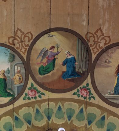 Zdjęcie nr 6: Polichromia malarska we wnętrzu drewnianego kościoła parafialnego w Polance Wielkiej zachowała się w prezbiterium, nawie oraz w przedsionku urządzonym w przyziemiu wieży. W prezbiterium i nawie zastosowano podział ramowy uwzględniający drewniane pilastry artykułujące ściany, gzyms oraz fasetę. Na ścianach pomiędzy pilastrami wprowadzono czworoboczne panneau o narożach utworzonych w stylizowanych formach nawiązujących do motywów roślinno-kwiatowych. Fasetę udekorowano rytmicznie rozłożonym ornamentem z motywów kwiatowych w formie dekoracyjnego fryzu, korespondującego z ornamentalną bordiurą poprowadzoną wzdłuż krawędzi płaskiego stropu. Na stropie w prezbiterium wyobrażono Trójcę Świętą, natomiast w nawie Matkę Boską Różańcową otoczoną przez tajemnice różańcowe w medalionach. Trójcę Świętą wyobrażono na obłokach na niebieskim tle usianym złotymi gwiazdkami. Frontalnie ujęty Bóg Ojciec został ukazany jako siwobrody starzec o bujnych siwych włosach. W prawej ręce trzyma złote berło, lewą zaś wyciąga przed siebie. Bóg Ojciec stopy wspiera o niebieski glob wyłaniający się z obłoków poniżej. Jego twarz charakteryzuje jasna karnacja, szeroko otwarte oczy, wydatny nos i usta. Głowę otacza długa, siwa broda i podobne włosy. Obok Boga Ojca z lewej strony siedzi Chrystus, który obie nogi wspiera na globie. Zbawiciel prawą ręką podtrzymuje oparty o ramię drewniany krzyż, lewą zaś ma odsuniętą od siebie. Jezus został przedstawiony w trzech czwartych w prawo. Jest to dojrzały mężczyzna o pociągłej twarzy okolonej brązowymi, długimi włosami spływającymi na ramiona oraz brodą. Ma jasną karnację, prosty nos i wydatne usta. Nagi tors okrywa bladoszkarłatny płaszcz odsłaniający prawą nogę. Na dłoniach i stopach widoczne są rany po gwoździach. Głowę Jezusa okala świetlisty nimb. Powyżej obu postaci na tle rozjaśnionego nieba unosi się gołębica Ducha Świętego w promienistym otoku. Polichromia stropu w nawie została zakomponowana w oparciu o zmniejszające się koncentryczne okręgi wpisane w dekoracjne panneau o narożach utworzonych ze stylizowanych form nawiązujących do motywów roślinno-kwiatowych. W środkowym okręgu ukazano zasiadającą na obłokach Matkę Boską z Dzieciątkiem otoczoną okrągłym obramieniem utworzonym z wielobarwnego ornamentu z motywem naprzemiennie ułożonych lancetowatych liści-łusek. Madonna została przedstawiona frontalnie, z prawą ręką przyłożoną do piersi, lewą zaś obejmuje Dzieciątko Jezus siedzące na globie ułożonym na kolanach matki podtrzymywanym przez anioła. Maryja ma pociągłą twarz o wydatnym nosie i wargach. Jej spojrzenie półprzymkniętych oczu skierowane jest pokornie ku dołowi. Głowę Marii otaczają, brązowe, falujące włosy spływające na ramiona. Madonna ubrana jest w czerwoną suknię przewiązaną złocistą szarfą w pasie i niebieski płaszcz lamowany złotą taśmą, spięty pod szyją z lewą połą osłaniającą jej kolana. Lewą stopę Matka Boska wspiera o wystający spod płaszcza poniżej złoty półksiężyc. Siedzące na globie Dzieciątko ujęte zostało w trzech czwartych w lewo. Mały Jezus prawą ręką nakłada matce złotą koronę, w lewej zaś trzyma lilię. Zbawiciel ma owalną twarz o jasnej karnacjim i rumianych policzkach z drobnym nosem i ustami. Jego głowę okalają jasne loki. Ubrany jest w jasną przepaskę przerzuconą przez prawe ramię oraz biodra. Głowy obu postaci otaczają świetliste promienie. Z prawej strony Marii stoi ujęty w trzech czwarty w prawo anioł, z twarzą zwróconą w stronę widza, podtrzymujący oburącz niebieski glob, na którym siedzi Jezus. Uskrzydlony anioł o jasnobrązowych włosach ubrany jest w zieloną tunikę przewiązaną w pasie. Za Madonną z lewej strony widoczny jest asystujący drugi anioł w cynobrowej tunice i jasnych włosach spływających na ramiona. Pod półksiężycem na tle obłoków widoczne są trzy uskrzydlone główki anielskie. Wokół Matki Boskiej rozmieszczono owalne medaliony z blachy miedzianej malowane w piętnaście tajemnic Różańca świętego. Ich narracja rozpoczyna się nad głową Madonny. Każda ze scen oparta jest o kilkuosobową kompozycję. Idąc w lewo namalowano: Zwiastowanie Marii, Nawiedzenie św. Elżbiety, Boże Narodzenie, Ofiarowanie w świątyni, Znalezienie w świątyni, Modlitwa w Ogrójcu, Biczowanie, Cierniem ukoronowanie, Niesienie krzyża, Ukrzyżowanie, Zmartwychwstanie, Wniebowstąpienie, Zesłanie Ducha Świętego, Wniebowzięcie Marii, Ukoronowanie Marii w niebie. Pomiędzy medalionami namalowano czerwone róże. Całoś obramienia ornamentalny okrąg. Dekorację w przedsionku utworzono za pomocą iluzjonistycznie malowanych cynobrowych kolumn o korynckich kapitelach ustawionych na wysokich postumentach, podtrzymujących belkowanie. Pomiędzy kolumnami ściany są gładkie, bladoniebieskie. Strop ozdobiono obramieniem w formie czworobocznego panneau o narożach utworzonych ze stylizowanych form nawiązujących do motywów roślinno-kwiatowych. 