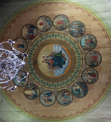 Zdjęcie nr 4: Polichromia malarska we wnętrzu drewnianego kościoła parafialnego w Polance Wielkiej zachowała się w prezbiterium, nawie oraz w przedsionku urządzonym w przyziemiu wieży. W prezbiterium i nawie zastosowano podział ramowy uwzględniający drewniane pilastry artykułujące ściany, gzyms oraz fasetę. Na ścianach pomiędzy pilastrami wprowadzono czworoboczne panneau o narożach utworzonych w stylizowanych formach nawiązujących do motywów roślinno-kwiatowych. Fasetę udekorowano rytmicznie rozłożonym ornamentem z motywów kwiatowych w formie dekoracyjnego fryzu, korespondującego z ornamentalną bordiurą poprowadzoną wzdłuż krawędzi płaskiego stropu. Na stropie w prezbiterium wyobrażono Trójcę Świętą, natomiast w nawie Matkę Boską Różańcową otoczoną przez tajemnice różańcowe w medalionach. Trójcę Świętą wyobrażono na obłokach na niebieskim tle usianym złotymi gwiazdkami. Frontalnie ujęty Bóg Ojciec został ukazany jako siwobrody starzec o bujnych siwych włosach. W prawej ręce trzyma złote berło, lewą zaś wyciąga przed siebie. Bóg Ojciec stopy wspiera o niebieski glob wyłaniający się z obłoków poniżej. Jego twarz charakteryzuje jasna karnacja, szeroko otwarte oczy, wydatny nos i usta. Głowę otacza długa, siwa broda i podobne włosy. Obok Boga Ojca z lewej strony siedzi Chrystus, który obie nogi wspiera na globie. Zbawiciel prawą ręką podtrzymuje oparty o ramię drewniany krzyż, lewą zaś ma odsuniętą od siebie. Jezus został przedstawiony w trzech czwartych w prawo. Jest to dojrzały mężczyzna o pociągłej twarzy okolonej brązowymi, długimi włosami spływającymi na ramiona oraz brodą. Ma jasną karnację, prosty nos i wydatne usta. Nagi tors okrywa bladoszkarłatny płaszcz odsłaniający prawą nogę. Na dłoniach i stopach widoczne są rany po gwoździach. Głowę Jezusa okala świetlisty nimb. Powyżej obu postaci na tle rozjaśnionego nieba unosi się gołębica Ducha Świętego w promienistym otoku. Polichromia stropu w nawie została zakomponowana w oparciu o zmniejszające się koncentryczne okręgi wpisane w dekoracjne panneau o narożach utworzonych ze stylizowanych form nawiązujących do motywów roślinno-kwiatowych. W środkowym okręgu ukazano zasiadającą na obłokach Matkę Boską z Dzieciątkiem otoczoną okrągłym obramieniem utworzonym z wielobarwnego ornamentu z motywem naprzemiennie ułożonych lancetowatych liści-łusek. Madonna została przedstawiona frontalnie, z prawą ręką przyłożoną do piersi, lewą zaś obejmuje Dzieciątko Jezus siedzące na globie ułożonym na kolanach matki podtrzymywanym przez anioła. Maryja ma pociągłą twarz o wydatnym nosie i wargach. Jej spojrzenie półprzymkniętych oczu skierowane jest pokornie ku dołowi. Głowę Marii otaczają, brązowe, falujące włosy spływające na ramiona. Madonna ubrana jest w czerwoną suknię przewiązaną złocistą szarfą w pasie i niebieski płaszcz lamowany złotą taśmą, spięty pod szyją z lewą połą osłaniającą jej kolana. Lewą stopę Matka Boska wspiera o wystający spod płaszcza poniżej złoty półksiężyc. Siedzące na globie Dzieciątko ujęte zostało w trzech czwartych w lewo. Mały Jezus prawą ręką nakłada matce złotą koronę, w lewej zaś trzyma lilię. Zbawiciel ma owalną twarz o jasnej karnacjim i rumianych policzkach z drobnym nosem i ustami. Jego głowę okalają jasne loki. Ubrany jest w jasną przepaskę przerzuconą przez prawe ramię oraz biodra. Głowy obu postaci otaczają świetliste promienie. Z prawej strony Marii stoi ujęty w trzech czwarty w prawo anioł, z twarzą zwróconą w stronę widza, podtrzymujący oburącz niebieski glob, na którym siedzi Jezus. Uskrzydlony anioł o jasnobrązowych włosach ubrany jest w zieloną tunikę przewiązaną w pasie. Za Madonną z lewej strony widoczny jest asystujący drugi anioł w cynobrowej tunice i jasnych włosach spływających na ramiona. Pod półksiężycem na tle obłoków widoczne są trzy uskrzydlone główki anielskie. Wokół Matki Boskiej rozmieszczono owalne medaliony z blachy miedzianej malowane w piętnaście tajemnic Różańca świętego. Ich narracja rozpoczyna się nad głową Madonny. Każda ze scen oparta jest o kilkuosobową kompozycję. Idąc w lewo namalowano: Zwiastowanie Marii, Nawiedzenie św. Elżbiety, Boże Narodzenie, Ofiarowanie w świątyni, Znalezienie w świątyni, Modlitwa w Ogrójcu, Biczowanie, Cierniem ukoronowanie, Niesienie krzyża, Ukrzyżowanie, Zmartwychwstanie, Wniebowstąpienie, Zesłanie Ducha Świętego, Wniebowzięcie Marii, Ukoronowanie Marii w niebie. Pomiędzy medalionami namalowano czerwone róże. Całoś obramienia ornamentalny okrąg. Dekorację w przedsionku utworzono za pomocą iluzjonistycznie malowanych cynobrowych kolumn o korynckich kapitelach ustawionych na wysokich postumentach, podtrzymujących belkowanie. Pomiędzy kolumnami ściany są gładkie, bladoniebieskie. Strop ozdobiono obramieniem w formie czworobocznego panneau o narożach utworzonych ze stylizowanych form nawiązujących do motywów roślinno-kwiatowych. 