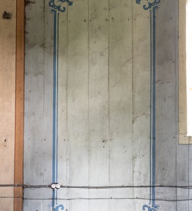 Zdjęcie nr 13: Polichromia malarska we wnętrzu drewnianego kościoła parafialnego w Polance Wielkiej zachowała się w prezbiterium, nawie oraz w przedsionku urządzonym w przyziemiu wieży. W prezbiterium i nawie zastosowano podział ramowy uwzględniający drewniane pilastry artykułujące ściany, gzyms oraz fasetę. Na ścianach pomiędzy pilastrami wprowadzono czworoboczne panneau o narożach utworzonych w stylizowanych formach nawiązujących do motywów roślinno-kwiatowych. Fasetę udekorowano rytmicznie rozłożonym ornamentem z motywów kwiatowych w formie dekoracyjnego fryzu, korespondującego z ornamentalną bordiurą poprowadzoną wzdłuż krawędzi płaskiego stropu. Na stropie w prezbiterium wyobrażono Trójcę Świętą, natomiast w nawie Matkę Boską Różańcową otoczoną przez tajemnice różańcowe w medalionach. Trójcę Świętą wyobrażono na obłokach na niebieskim tle usianym złotymi gwiazdkami. Frontalnie ujęty Bóg Ojciec został ukazany jako siwobrody starzec o bujnych siwych włosach. W prawej ręce trzyma złote berło, lewą zaś wyciąga przed siebie. Bóg Ojciec stopy wspiera o niebieski glob wyłaniający się z obłoków poniżej. Jego twarz charakteryzuje jasna karnacja, szeroko otwarte oczy, wydatny nos i usta. Głowę otacza długa, siwa broda i podobne włosy. Obok Boga Ojca z lewej strony siedzi Chrystus, który obie nogi wspiera na globie. Zbawiciel prawą ręką podtrzymuje oparty o ramię drewniany krzyż, lewą zaś ma odsuniętą od siebie. Jezus został przedstawiony w trzech czwartych w prawo. Jest to dojrzały mężczyzna o pociągłej twarzy okolonej brązowymi, długimi włosami spływającymi na ramiona oraz brodą. Ma jasną karnację, prosty nos i wydatne usta. Nagi tors okrywa bladoszkarłatny płaszcz odsłaniający prawą nogę. Na dłoniach i stopach widoczne są rany po gwoździach. Głowę Jezusa okala świetlisty nimb. Powyżej obu postaci na tle rozjaśnionego nieba unosi się gołębica Ducha Świętego w promienistym otoku. Polichromia stropu w nawie została zakomponowana w oparciu o zmniejszające się koncentryczne okręgi wpisane w dekoracjne panneau o narożach utworzonych ze stylizowanych form nawiązujących do motywów roślinno-kwiatowych. W środkowym okręgu ukazano zasiadającą na obłokach Matkę Boską z Dzieciątkiem otoczoną okrągłym obramieniem utworzonym z wielobarwnego ornamentu z motywem naprzemiennie ułożonych lancetowatych liści-łusek. Madonna została przedstawiona frontalnie, z prawą ręką przyłożoną do piersi, lewą zaś obejmuje Dzieciątko Jezus siedzące na globie ułożonym na kolanach matki podtrzymywanym przez anioła. Maryja ma pociągłą twarz o wydatnym nosie i wargach. Jej spojrzenie półprzymkniętych oczu skierowane jest pokornie ku dołowi. Głowę Marii otaczają, brązowe, falujące włosy spływające na ramiona. Madonna ubrana jest w czerwoną suknię przewiązaną złocistą szarfą w pasie i niebieski płaszcz lamowany złotą taśmą, spięty pod szyją z lewą połą osłaniającą jej kolana. Lewą stopę Matka Boska wspiera o wystający spod płaszcza poniżej złoty półksiężyc. Siedzące na globie Dzieciątko ujęte zostało w trzech czwartych w lewo. Mały Jezus prawą ręką nakłada matce złotą koronę, w lewej zaś trzyma lilię. Zbawiciel ma owalną twarz o jasnej karnacjim i rumianych policzkach z drobnym nosem i ustami. Jego głowę okalają jasne loki. Ubrany jest w jasną przepaskę przerzuconą przez prawe ramię oraz biodra. Głowy obu postaci otaczają świetliste promienie. Z prawej strony Marii stoi ujęty w trzech czwarty w prawo anioł, z twarzą zwróconą w stronę widza, podtrzymujący oburącz niebieski glob, na którym siedzi Jezus. Uskrzydlony anioł o jasnobrązowych włosach ubrany jest w zieloną tunikę przewiązaną w pasie. Za Madonną z lewej strony widoczny jest asystujący drugi anioł w cynobrowej tunice i jasnych włosach spływających na ramiona. Pod półksiężycem na tle obłoków widoczne są trzy uskrzydlone główki anielskie. Wokół Matki Boskiej rozmieszczono owalne medaliony z blachy miedzianej malowane w piętnaście tajemnic Różańca świętego. Ich narracja rozpoczyna się nad głową Madonny. Każda ze scen oparta jest o kilkuosobową kompozycję. Idąc w lewo namalowano: Zwiastowanie Marii, Nawiedzenie św. Elżbiety, Boże Narodzenie, Ofiarowanie w świątyni, Znalezienie w świątyni, Modlitwa w Ogrójcu, Biczowanie, Cierniem ukoronowanie, Niesienie krzyża, Ukrzyżowanie, Zmartwychwstanie, Wniebowstąpienie, Zesłanie Ducha Świętego, Wniebowzięcie Marii, Ukoronowanie Marii w niebie. Pomiędzy medalionami namalowano czerwone róże. Całoś obramienia ornamentalny okrąg. Dekorację w przedsionku utworzono za pomocą iluzjonistycznie malowanych cynobrowych kolumn o korynckich kapitelach ustawionych na wysokich postumentach, podtrzymujących belkowanie. Pomiędzy kolumnami ściany są gładkie, bladoniebieskie. Strop ozdobiono obramieniem w formie czworobocznego panneau o narożach utworzonych ze stylizowanych form nawiązujących do motywów roślinno-kwiatowych. 