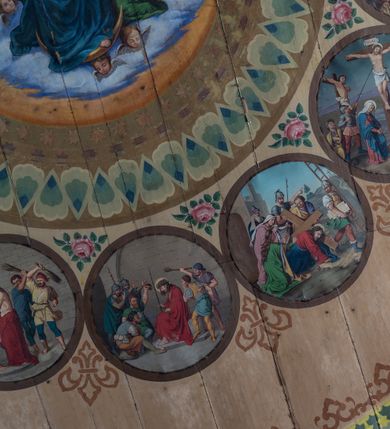 Zdjęcie nr 11: Polichromia malarska we wnętrzu drewnianego kościoła parafialnego w Polance Wielkiej zachowała się w prezbiterium, nawie oraz w przedsionku urządzonym w przyziemiu wieży. W prezbiterium i nawie zastosowano podział ramowy uwzględniający drewniane pilastry artykułujące ściany, gzyms oraz fasetę. Na ścianach pomiędzy pilastrami wprowadzono czworoboczne panneau o narożach utworzonych w stylizowanych formach nawiązujących do motywów roślinno-kwiatowych. Fasetę udekorowano rytmicznie rozłożonym ornamentem z motywów kwiatowych w formie dekoracyjnego fryzu, korespondującego z ornamentalną bordiurą poprowadzoną wzdłuż krawędzi płaskiego stropu. Na stropie w prezbiterium wyobrażono Trójcę Świętą, natomiast w nawie Matkę Boską Różańcową otoczoną przez tajemnice różańcowe w medalionach. Trójcę Świętą wyobrażono na obłokach na niebieskim tle usianym złotymi gwiazdkami. Frontalnie ujęty Bóg Ojciec został ukazany jako siwobrody starzec o bujnych siwych włosach. W prawej ręce trzyma złote berło, lewą zaś wyciąga przed siebie. Bóg Ojciec stopy wspiera o niebieski glob wyłaniający się z obłoków poniżej. Jego twarz charakteryzuje jasna karnacja, szeroko otwarte oczy, wydatny nos i usta. Głowę otacza długa, siwa broda i podobne włosy. Obok Boga Ojca z lewej strony siedzi Chrystus, który obie nogi wspiera na globie. Zbawiciel prawą ręką podtrzymuje oparty o ramię drewniany krzyż, lewą zaś ma odsuniętą od siebie. Jezus został przedstawiony w trzech czwartych w prawo. Jest to dojrzały mężczyzna o pociągłej twarzy okolonej brązowymi, długimi włosami spływającymi na ramiona oraz brodą. Ma jasną karnację, prosty nos i wydatne usta. Nagi tors okrywa bladoszkarłatny płaszcz odsłaniający prawą nogę. Na dłoniach i stopach widoczne są rany po gwoździach. Głowę Jezusa okala świetlisty nimb. Powyżej obu postaci na tle rozjaśnionego nieba unosi się gołębica Ducha Świętego w promienistym otoku. Polichromia stropu w nawie została zakomponowana w oparciu o zmniejszające się koncentryczne okręgi wpisane w dekoracjne panneau o narożach utworzonych ze stylizowanych form nawiązujących do motywów roślinno-kwiatowych. W środkowym okręgu ukazano zasiadającą na obłokach Matkę Boską z Dzieciątkiem otoczoną okrągłym obramieniem utworzonym z wielobarwnego ornamentu z motywem naprzemiennie ułożonych lancetowatych liści-łusek. Madonna została przedstawiona frontalnie, z prawą ręką przyłożoną do piersi, lewą zaś obejmuje Dzieciątko Jezus siedzące na globie ułożonym na kolanach matki podtrzymywanym przez anioła. Maryja ma pociągłą twarz o wydatnym nosie i wargach. Jej spojrzenie półprzymkniętych oczu skierowane jest pokornie ku dołowi. Głowę Marii otaczają, brązowe, falujące włosy spływające na ramiona. Madonna ubrana jest w czerwoną suknię przewiązaną złocistą szarfą w pasie i niebieski płaszcz lamowany złotą taśmą, spięty pod szyją z lewą połą osłaniającą jej kolana. Lewą stopę Matka Boska wspiera o wystający spod płaszcza poniżej złoty półksiężyc. Siedzące na globie Dzieciątko ujęte zostało w trzech czwartych w lewo. Mały Jezus prawą ręką nakłada matce złotą koronę, w lewej zaś trzyma lilię. Zbawiciel ma owalną twarz o jasnej karnacjim i rumianych policzkach z drobnym nosem i ustami. Jego głowę okalają jasne loki. Ubrany jest w jasną przepaskę przerzuconą przez prawe ramię oraz biodra. Głowy obu postaci otaczają świetliste promienie. Z prawej strony Marii stoi ujęty w trzech czwarty w prawo anioł, z twarzą zwróconą w stronę widza, podtrzymujący oburącz niebieski glob, na którym siedzi Jezus. Uskrzydlony anioł o jasnobrązowych włosach ubrany jest w zieloną tunikę przewiązaną w pasie. Za Madonną z lewej strony widoczny jest asystujący drugi anioł w cynobrowej tunice i jasnych włosach spływających na ramiona. Pod półksiężycem na tle obłoków widoczne są trzy uskrzydlone główki anielskie. Wokół Matki Boskiej rozmieszczono owalne medaliony z blachy miedzianej malowane w piętnaście tajemnic Różańca świętego. Ich narracja rozpoczyna się nad głową Madonny. Każda ze scen oparta jest o kilkuosobową kompozycję. Idąc w lewo namalowano: Zwiastowanie Marii, Nawiedzenie św. Elżbiety, Boże Narodzenie, Ofiarowanie w świątyni, Znalezienie w świątyni, Modlitwa w Ogrójcu, Biczowanie, Cierniem ukoronowanie, Niesienie krzyża, Ukrzyżowanie, Zmartwychwstanie, Wniebowstąpienie, Zesłanie Ducha Świętego, Wniebowzięcie Marii, Ukoronowanie Marii w niebie. Pomiędzy medalionami namalowano czerwone róże. Całoś obramienia ornamentalny okrąg. Dekorację w przedsionku utworzono za pomocą iluzjonistycznie malowanych cynobrowych kolumn o korynckich kapitelach ustawionych na wysokich postumentach, podtrzymujących belkowanie. Pomiędzy kolumnami ściany są gładkie, bladoniebieskie. Strop ozdobiono obramieniem w formie czworobocznego panneau o narożach utworzonych ze stylizowanych form nawiązujących do motywów roślinno-kwiatowych. 