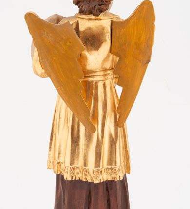 Zdjęcie nr 6: Figura pełnoplastyczna, ustawiona na niskiej podstawie. Postać ukazana frontalnie, z głową skierowaną w prawo, w kontrapoście, z obiema rękami uniesionymi z przodu, jedną wysoko, drugą nisko. Twarz ma podłużną, z drugim podbródkiem, o dużych, migdałowatych i opadających oczach, wąskim nosie i ustach, okoloną krótkimi, kręconymi włosami, układającymi się w czub nad czołem. Anioł ubrany jest w ciemnoczerwoną suknię spodnią i złoconą suknię wierzchnią, sięgającą kolan, z podwiniętymi rękawami, przepasaną w talii szarfą. Skrzydła ma złocone, złożone na plecach. Polichromia ciała naturalistyczna. 