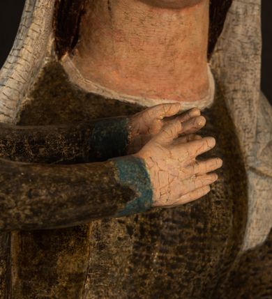 Zdjęcie nr 15: Stojąca figura Matki Boskiej z Dzieciątkiem reprezentuje przykład przyściennej rzeźby z tyłu wydrążonej. Maria stoi w lekkim kontrapoście, podkreślonym wysunięciem do przodu lewego kolana na niewielkim wzgórku. Prawą ręką podtrzymuje Dzieciątko, w lewej dłoni trzyma jabłko. Madonna ma mocno pociągłą twarz o jasnej karnacji z wysokim czołem, rumianych policzkach, długi, prosty nos i wydatne usta. Jej głowa osadzona jest na długiej szyi. Spod białej chusty ubranej na głowę i opadającej na ramiona widać brązowe włosy. Matka Boska na głowie ma koronę o ostrych, krótkich sterczynach. Nałożony na ciemnooliwkową suknię płaszcz w tym samym kolorze, podbity błękitem, tworzy dwa wałkowate zaokrąglone fałdy na brzuchu Marii, spływając miękkimi fałdami spod lewej ręki oraz festonem spod prawej ręki. Niżej fałdy płaszcza i sukni układają się niemal pionowo, opinając materią lewą nogę. Długa suknia odsłania czubki ciżemek. Dzieciątko zostało ujęte w trzech czwartych w prawo. Obie jego rączki wyciągnięte są przed siebie w stronę trzymanego przez Marię jabłka. Z kolei nóżki są skrzyżowane przy stopach. Jezus ma wyrazistą twarz o jasnej karnacji, małym nosem i wydatnych ustach. Jego głowę otaczają brązowe włosy układające się po bokach w charakterystyczne pukle. Jezus ubrany jest w długą, ciemnooliwkową tunikę odsłaniającą fragmenty stóp z charakterystycznymi mankietami przy rękawach. Szaty Matki Boskiej i Dzieciątka są srebrzone i laserowane.