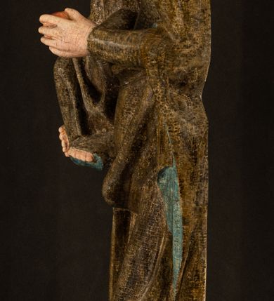 Zdjęcie nr 25: Stojąca figura Matki Boskiej z Dzieciątkiem reprezentuje przykład przyściennej rzeźby z tyłu wydrążonej. Maria stoi w lekkim kontrapoście, podkreślonym wysunięciem do przodu lewego kolana na niewielkim wzgórku. Prawą ręką podtrzymuje Dzieciątko, w lewej dłoni trzyma jabłko. Madonna ma mocno pociągłą twarz o jasnej karnacji z wysokim czołem, rumianych policzkach, długi, prosty nos i wydatne usta. Jej głowa osadzona jest na długiej szyi. Spod białej chusty ubranej na głowę i opadającej na ramiona widać brązowe włosy. Matka Boska na głowie ma koronę o ostrych, krótkich sterczynach. Nałożony na ciemnooliwkową suknię płaszcz w tym samym kolorze, podbity błękitem, tworzy dwa wałkowate zaokrąglone fałdy na brzuchu Marii, spływając miękkimi fałdami spod lewej ręki oraz festonem spod prawej ręki. Niżej fałdy płaszcza i sukni układają się niemal pionowo, opinając materią lewą nogę. Długa suknia odsłania czubki ciżemek. Dzieciątko zostało ujęte w trzech czwartych w prawo. Obie jego rączki wyciągnięte są przed siebie w stronę trzymanego przez Marię jabłka. Z kolei nóżki są skrzyżowane przy stopach. Jezus ma wyrazistą twarz o jasnej karnacji, małym nosem i wydatnych ustach. Jego głowę otaczają brązowe włosy układające się po bokach w charakterystyczne pukle. Jezus ubrany jest w długą, ciemnooliwkową tunikę odsłaniającą fragmenty stóp z charakterystycznymi mankietami przy rękawach. Szaty Matki Boskiej i Dzieciątka są srebrzone i laserowane.