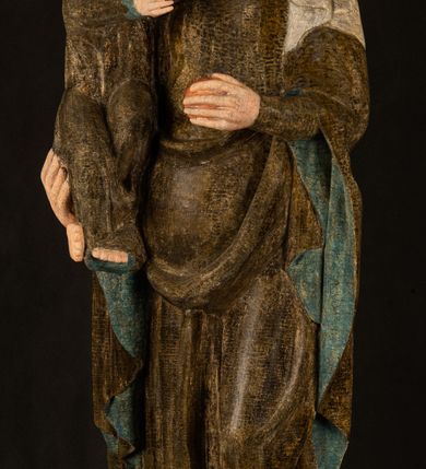 Zdjęcie nr 2: Stojąca figura Matki Boskiej z Dzieciątkiem reprezentuje przykład przyściennej rzeźby z tyłu wydrążonej. Maria stoi w lekkim kontrapoście, podkreślonym wysunięciem do przodu lewego kolana na niewielkim wzgórku. Prawą ręką podtrzymuje Dzieciątko, w lewej dłoni trzyma jabłko. Madonna ma mocno pociągłą twarz o jasnej karnacji z wysokim czołem, rumianych policzkach, długi, prosty nos i wydatne usta. Jej głowa osadzona jest na długiej szyi. Spod białej chusty ubranej na głowę i opadającej na ramiona widać brązowe włosy. Matka Boska na głowie ma koronę o ostrych, krótkich sterczynach. Nałożony na ciemnooliwkową suknię płaszcz w tym samym kolorze, podbity błękitem, tworzy dwa wałkowate zaokrąglone fałdy na brzuchu Marii, spływając miękkimi fałdami spod lewej ręki oraz festonem spod prawej ręki. Niżej fałdy płaszcza i sukni układają się niemal pionowo, opinając materią lewą nogę. Długa suknia odsłania czubki ciżemek. Dzieciątko zostało ujęte w trzech czwartych w prawo. Obie jego rączki wyciągnięte są przed siebie w stronę trzymanego przez Marię jabłka. Z kolei nóżki są skrzyżowane przy stopach. Jezus ma wyrazistą twarz o jasnej karnacji, małym nosem i wydatnych ustach. Jego głowę otaczają brązowe włosy układające się po bokach w charakterystyczne pukle. Jezus ubrany jest w długą, ciemnooliwkową tunikę odsłaniającą fragmenty stóp z charakterystycznymi mankietami przy rękawach. Szaty Matki Boskiej i Dzieciątka są srebrzone i laserowane.