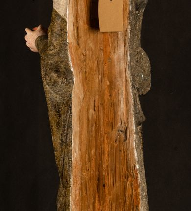 Zdjęcie nr 26: Stojąca figura Matki Boskiej z Dzieciątkiem reprezentuje przykład przyściennej rzeźby z tyłu wydrążonej. Maria stoi w lekkim kontrapoście, podkreślonym wysunięciem do przodu lewego kolana na niewielkim wzgórku. Prawą ręką podtrzymuje Dzieciątko, w lewej dłoni trzyma jabłko. Madonna ma mocno pociągłą twarz o jasnej karnacji z wysokim czołem, rumianych policzkach, długi, prosty nos i wydatne usta. Jej głowa osadzona jest na długiej szyi. Spod białej chusty ubranej na głowę i opadającej na ramiona widać brązowe włosy. Matka Boska na głowie ma koronę o ostrych, krótkich sterczynach. Nałożony na ciemnooliwkową suknię płaszcz w tym samym kolorze, podbity błękitem, tworzy dwa wałkowate zaokrąglone fałdy na brzuchu Marii, spływając miękkimi fałdami spod lewej ręki oraz festonem spod prawej ręki. Niżej fałdy płaszcza i sukni układają się niemal pionowo, opinając materią lewą nogę. Długa suknia odsłania czubki ciżemek. Dzieciątko zostało ujęte w trzech czwartych w prawo. Obie jego rączki wyciągnięte są przed siebie w stronę trzymanego przez Marię jabłka. Z kolei nóżki są skrzyżowane przy stopach. Jezus ma wyrazistą twarz o jasnej karnacji, małym nosem i wydatnych ustach. Jego głowę otaczają brązowe włosy układające się po bokach w charakterystyczne pukle. Jezus ubrany jest w długą, ciemnooliwkową tunikę odsłaniającą fragmenty stóp z charakterystycznymi mankietami przy rękawach. Szaty Matki Boskiej i Dzieciątka są srebrzone i laserowane.