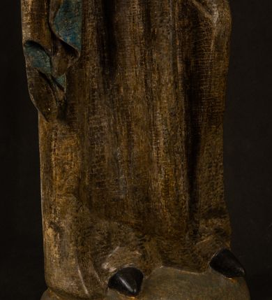 Zdjęcie nr 4: Stojąca figura Matki Boskiej z Dzieciątkiem reprezentuje przykład przyściennej rzeźby z tyłu wydrążonej. Maria stoi w lekkim kontrapoście, podkreślonym wysunięciem do przodu lewego kolana na niewielkim wzgórku. Prawą ręką podtrzymuje Dzieciątko, w lewej dłoni trzyma jabłko. Madonna ma mocno pociągłą twarz o jasnej karnacji z wysokim czołem, rumianych policzkach, długi, prosty nos i wydatne usta. Jej głowa osadzona jest na długiej szyi. Spod białej chusty ubranej na głowę i opadającej na ramiona widać brązowe włosy. Matka Boska na głowie ma koronę o ostrych, krótkich sterczynach. Nałożony na ciemnooliwkową suknię płaszcz w tym samym kolorze, podbity błękitem, tworzy dwa wałkowate zaokrąglone fałdy na brzuchu Marii, spływając miękkimi fałdami spod lewej ręki oraz festonem spod prawej ręki. Niżej fałdy płaszcza i sukni układają się niemal pionowo, opinając materią lewą nogę. Długa suknia odsłania czubki ciżemek. Dzieciątko zostało ujęte w trzech czwartych w prawo. Obie jego rączki wyciągnięte są przed siebie w stronę trzymanego przez Marię jabłka. Z kolei nóżki są skrzyżowane przy stopach. Jezus ma wyrazistą twarz o jasnej karnacji, małym nosem i wydatnych ustach. Jego głowę otaczają brązowe włosy układające się po bokach w charakterystyczne pukle. Jezus ubrany jest w długą, ciemnooliwkową tunikę odsłaniającą fragmenty stóp z charakterystycznymi mankietami przy rękawach. Szaty Matki Boskiej i Dzieciątka są srebrzone i laserowane.