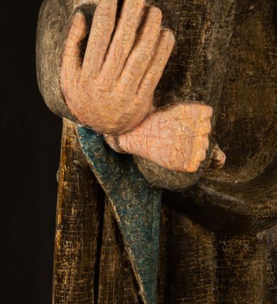 Zdjęcie nr 12: Stojąca figura Matki Boskiej z Dzieciątkiem reprezentuje przykład przyściennej rzeźby z tyłu wydrążonej. Maria stoi w lekkim kontrapoście, podkreślonym wysunięciem do przodu lewego kolana na niewielkim wzgórku. Prawą ręką podtrzymuje Dzieciątko, w lewej dłoni trzyma jabłko. Madonna ma mocno pociągłą twarz o jasnej karnacji z wysokim czołem, rumianych policzkach, długi, prosty nos i wydatne usta. Jej głowa osadzona jest na długiej szyi. Spod białej chusty ubranej na głowę i opadającej na ramiona widać brązowe włosy. Matka Boska na głowie ma koronę o ostrych, krótkich sterczynach. Nałożony na ciemnooliwkową suknię płaszcz w tym samym kolorze, podbity błękitem, tworzy dwa wałkowate zaokrąglone fałdy na brzuchu Marii, spływając miękkimi fałdami spod lewej ręki oraz festonem spod prawej ręki. Niżej fałdy płaszcza i sukni układają się niemal pionowo, opinając materią lewą nogę. Długa suknia odsłania czubki ciżemek. Dzieciątko zostało ujęte w trzech czwartych w prawo. Obie jego rączki wyciągnięte są przed siebie w stronę trzymanego przez Marię jabłka. Z kolei nóżki są skrzyżowane przy stopach. Jezus ma wyrazistą twarz o jasnej karnacji, małym nosem i wydatnych ustach. Jego głowę otaczają brązowe włosy układające się po bokach w charakterystyczne pukle. Jezus ubrany jest w długą, ciemnooliwkową tunikę odsłaniającą fragmenty stóp z charakterystycznymi mankietami przy rękawach. Szaty Matki Boskiej i Dzieciątka są srebrzone i laserowane.