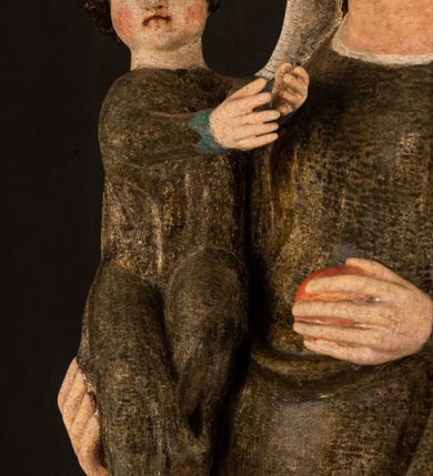 Zdjęcie nr 9: Stojąca figura Matki Boskiej z Dzieciątkiem reprezentuje przykład przyściennej rzeźby z tyłu wydrążonej. Maria stoi w lekkim kontrapoście, podkreślonym wysunięciem do przodu lewego kolana na niewielkim wzgórku. Prawą ręką podtrzymuje Dzieciątko, w lewej dłoni trzyma jabłko. Madonna ma mocno pociągłą twarz o jasnej karnacji z wysokim czołem, rumianych policzkach, długi, prosty nos i wydatne usta. Jej głowa osadzona jest na długiej szyi. Spod białej chusty ubranej na głowę i opadającej na ramiona widać brązowe włosy. Matka Boska na głowie ma koronę o ostrych, krótkich sterczynach. Nałożony na ciemnooliwkową suknię płaszcz w tym samym kolorze, podbity błękitem, tworzy dwa wałkowate zaokrąglone fałdy na brzuchu Marii, spływając miękkimi fałdami spod lewej ręki oraz festonem spod prawej ręki. Niżej fałdy płaszcza i sukni układają się niemal pionowo, opinając materią lewą nogę. Długa suknia odsłania czubki ciżemek. Dzieciątko zostało ujęte w trzech czwartych w prawo. Obie jego rączki wyciągnięte są przed siebie w stronę trzymanego przez Marię jabłka. Z kolei nóżki są skrzyżowane przy stopach. Jezus ma wyrazistą twarz o jasnej karnacji, małym nosem i wydatnych ustach. Jego głowę otaczają brązowe włosy układające się po bokach w charakterystyczne pukle. Jezus ubrany jest w długą, ciemnooliwkową tunikę odsłaniającą fragmenty stóp z charakterystycznymi mankietami przy rękawach. Szaty Matki Boskiej i Dzieciątka są srebrzone i laserowane.