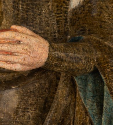 Zdjęcie nr 14: Stojąca figura Matki Boskiej z Dzieciątkiem reprezentuje przykład przyściennej rzeźby z tyłu wydrążonej. Maria stoi w lekkim kontrapoście, podkreślonym wysunięciem do przodu lewego kolana na niewielkim wzgórku. Prawą ręką podtrzymuje Dzieciątko, w lewej dłoni trzyma jabłko. Madonna ma mocno pociągłą twarz o jasnej karnacji z wysokim czołem, rumianych policzkach, długi, prosty nos i wydatne usta. Jej głowa osadzona jest na długiej szyi. Spod białej chusty ubranej na głowę i opadającej na ramiona widać brązowe włosy. Matka Boska na głowie ma koronę o ostrych, krótkich sterczynach. Nałożony na ciemnooliwkową suknię płaszcz w tym samym kolorze, podbity błękitem, tworzy dwa wałkowate zaokrąglone fałdy na brzuchu Marii, spływając miękkimi fałdami spod lewej ręki oraz festonem spod prawej ręki. Niżej fałdy płaszcza i sukni układają się niemal pionowo, opinając materią lewą nogę. Długa suknia odsłania czubki ciżemek. Dzieciątko zostało ujęte w trzech czwartych w prawo. Obie jego rączki wyciągnięte są przed siebie w stronę trzymanego przez Marię jabłka. Z kolei nóżki są skrzyżowane przy stopach. Jezus ma wyrazistą twarz o jasnej karnacji, małym nosem i wydatnych ustach. Jego głowę otaczają brązowe włosy układające się po bokach w charakterystyczne pukle. Jezus ubrany jest w długą, ciemnooliwkową tunikę odsłaniającą fragmenty stóp z charakterystycznymi mankietami przy rękawach. Szaty Matki Boskiej i Dzieciątka są srebrzone i laserowane.