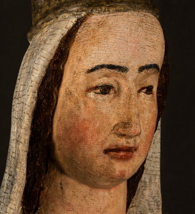 Zdjęcie nr 18: Stojąca figura Matki Boskiej z Dzieciątkiem reprezentuje przykład przyściennej rzeźby z tyłu wydrążonej. Maria stoi w lekkim kontrapoście, podkreślonym wysunięciem do przodu lewego kolana na niewielkim wzgórku. Prawą ręką podtrzymuje Dzieciątko, w lewej dłoni trzyma jabłko. Madonna ma mocno pociągłą twarz o jasnej karnacji z wysokim czołem, rumianych policzkach, długi, prosty nos i wydatne usta. Jej głowa osadzona jest na długiej szyi. Spod białej chusty ubranej na głowę i opadającej na ramiona widać brązowe włosy. Matka Boska na głowie ma koronę o ostrych, krótkich sterczynach. Nałożony na ciemnooliwkową suknię płaszcz w tym samym kolorze, podbity błękitem, tworzy dwa wałkowate zaokrąglone fałdy na brzuchu Marii, spływając miękkimi fałdami spod lewej ręki oraz festonem spod prawej ręki. Niżej fałdy płaszcza i sukni układają się niemal pionowo, opinając materią lewą nogę. Długa suknia odsłania czubki ciżemek. Dzieciątko zostało ujęte w trzech czwartych w prawo. Obie jego rączki wyciągnięte są przed siebie w stronę trzymanego przez Marię jabłka. Z kolei nóżki są skrzyżowane przy stopach. Jezus ma wyrazistą twarz o jasnej karnacji, małym nosem i wydatnych ustach. Jego głowę otaczają brązowe włosy układające się po bokach w charakterystyczne pukle. Jezus ubrany jest w długą, ciemnooliwkową tunikę odsłaniającą fragmenty stóp z charakterystycznymi mankietami przy rękawach. Szaty Matki Boskiej i Dzieciątka są srebrzone i laserowane.