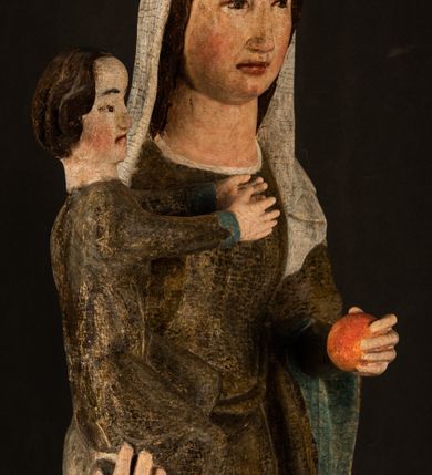 Zdjęcie nr 6: Stojąca figura Matki Boskiej z Dzieciątkiem reprezentuje przykład przyściennej rzeźby z tyłu wydrążonej. Maria stoi w lekkim kontrapoście, podkreślonym wysunięciem do przodu lewego kolana na niewielkim wzgórku. Prawą ręką podtrzymuje Dzieciątko, w lewej dłoni trzyma jabłko. Madonna ma mocno pociągłą twarz o jasnej karnacji z wysokim czołem, rumianych policzkach, długi, prosty nos i wydatne usta. Jej głowa osadzona jest na długiej szyi. Spod białej chusty ubranej na głowę i opadającej na ramiona widać brązowe włosy. Matka Boska na głowie ma koronę o ostrych, krótkich sterczynach. Nałożony na ciemnooliwkową suknię płaszcz w tym samym kolorze, podbity błękitem, tworzy dwa wałkowate zaokrąglone fałdy na brzuchu Marii, spływając miękkimi fałdami spod lewej ręki oraz festonem spod prawej ręki. Niżej fałdy płaszcza i sukni układają się niemal pionowo, opinając materią lewą nogę. Długa suknia odsłania czubki ciżemek. Dzieciątko zostało ujęte w trzech czwartych w prawo. Obie jego rączki wyciągnięte są przed siebie w stronę trzymanego przez Marię jabłka. Z kolei nóżki są skrzyżowane przy stopach. Jezus ma wyrazistą twarz o jasnej karnacji, małym nosem i wydatnych ustach. Jego głowę otaczają brązowe włosy układające się po bokach w charakterystyczne pukle. Jezus ubrany jest w długą, ciemnooliwkową tunikę odsłaniającą fragmenty stóp z charakterystycznymi mankietami przy rękawach. Szaty Matki Boskiej i Dzieciątka są srebrzone i laserowane.