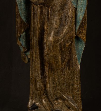 Zdjęcie nr 29: Stojąca figura Matki Boskiej z Dzieciątkiem reprezentuje przykład przyściennej rzeźby z tyłu wydrążonej. Maria stoi w lekkim kontrapoście, podkreślonym wysunięciem do przodu lewego kolana na niewielkim wzgórku. Prawą ręką podtrzymuje Dzieciątko, w lewej dłoni trzyma jabłko. Madonna ma mocno pociągłą twarz o jasnej karnacji z wysokim czołem, rumianych policzkach, długi, prosty nos i wydatne usta. Jej głowa osadzona jest na długiej szyi. Spod białej chusty ubranej na głowę i opadającej na ramiona widać brązowe włosy. Matka Boska na głowie ma koronę o ostrych, krótkich sterczynach. Nałożony na ciemnooliwkową suknię płaszcz w tym samym kolorze, podbity błękitem, tworzy dwa wałkowate zaokrąglone fałdy na brzuchu Marii, spływając miękkimi fałdami spod lewej ręki oraz festonem spod prawej ręki. Niżej fałdy płaszcza i sukni układają się niemal pionowo, opinając materią lewą nogę. Długa suknia odsłania czubki ciżemek. Dzieciątko zostało ujęte w trzech czwartych w prawo. Obie jego rączki wyciągnięte są przed siebie w stronę trzymanego przez Marię jabłka. Z kolei nóżki są skrzyżowane przy stopach. Jezus ma wyrazistą twarz o jasnej karnacji, małym nosem i wydatnych ustach. Jego głowę otaczają brązowe włosy układające się po bokach w charakterystyczne pukle. Jezus ubrany jest w długą, ciemnooliwkową tunikę odsłaniającą fragmenty stóp z charakterystycznymi mankietami przy rękawach. Szaty Matki Boskiej i Dzieciątka są srebrzone i laserowane.