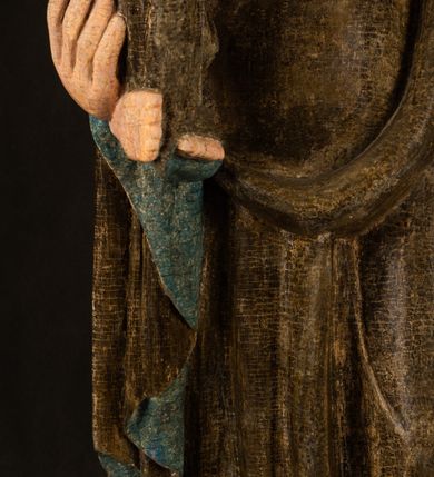 Zdjęcie nr 11: Stojąca figura Matki Boskiej z Dzieciątkiem reprezentuje przykład przyściennej rzeźby z tyłu wydrążonej. Maria stoi w lekkim kontrapoście, podkreślonym wysunięciem do przodu lewego kolana na niewielkim wzgórku. Prawą ręką podtrzymuje Dzieciątko, w lewej dłoni trzyma jabłko. Madonna ma mocno pociągłą twarz o jasnej karnacji z wysokim czołem, rumianych policzkach, długi, prosty nos i wydatne usta. Jej głowa osadzona jest na długiej szyi. Spod białej chusty ubranej na głowę i opadającej na ramiona widać brązowe włosy. Matka Boska na głowie ma koronę o ostrych, krótkich sterczynach. Nałożony na ciemnooliwkową suknię płaszcz w tym samym kolorze, podbity błękitem, tworzy dwa wałkowate zaokrąglone fałdy na brzuchu Marii, spływając miękkimi fałdami spod lewej ręki oraz festonem spod prawej ręki. Niżej fałdy płaszcza i sukni układają się niemal pionowo, opinając materią lewą nogę. Długa suknia odsłania czubki ciżemek. Dzieciątko zostało ujęte w trzech czwartych w prawo. Obie jego rączki wyciągnięte są przed siebie w stronę trzymanego przez Marię jabłka. Z kolei nóżki są skrzyżowane przy stopach. Jezus ma wyrazistą twarz o jasnej karnacji, małym nosem i wydatnych ustach. Jego głowę otaczają brązowe włosy układające się po bokach w charakterystyczne pukle. Jezus ubrany jest w długą, ciemnooliwkową tunikę odsłaniającą fragmenty stóp z charakterystycznymi mankietami przy rękawach. Szaty Matki Boskiej i Dzieciątka są srebrzone i laserowane.