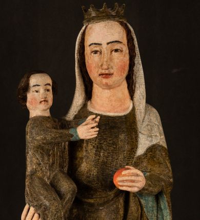 Zdjęcie nr 1: Stojąca figura Matki Boskiej z Dzieciątkiem reprezentuje przykład przyściennej rzeźby z tyłu wydrążonej. Maria stoi w lekkim kontrapoście, podkreślonym wysunięciem do przodu lewego kolana na niewielkim wzgórku. Prawą ręką podtrzymuje Dzieciątko, w lewej dłoni trzyma jabłko. Madonna ma mocno pociągłą twarz o jasnej karnacji z wysokim czołem, rumianych policzkach, długi, prosty nos i wydatne usta. Jej głowa osadzona jest na długiej szyi. Spod białej chusty ubranej na głowę i opadającej na ramiona widać brązowe włosy. Matka Boska na głowie ma koronę o ostrych, krótkich sterczynach. Nałożony na ciemnooliwkową suknię płaszcz w tym samym kolorze, podbity błękitem, tworzy dwa wałkowate zaokrąglone fałdy na brzuchu Marii, spływając miękkimi fałdami spod lewej ręki oraz festonem spod prawej ręki. Niżej fałdy płaszcza i sukni układają się niemal pionowo, opinając materią lewą nogę. Długa suknia odsłania czubki ciżemek. Dzieciątko zostało ujęte w trzech czwartych w prawo. Obie jego rączki wyciągnięte są przed siebie w stronę trzymanego przez Marię jabłka. Z kolei nóżki są skrzyżowane przy stopach. Jezus ma wyrazistą twarz o jasnej karnacji, małym nosem i wydatnych ustach. Jego głowę otaczają brązowe włosy układające się po bokach w charakterystyczne pukle. Jezus ubrany jest w długą, ciemnooliwkową tunikę odsłaniającą fragmenty stóp z charakterystycznymi mankietami przy rękawach. Szaty Matki Boskiej i Dzieciątka są srebrzone i laserowane.