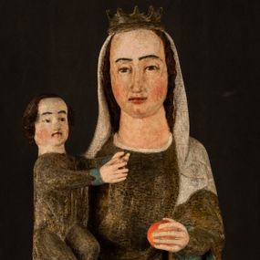 Zdjęcie nr 1: Stojąca figura Matki Boskiej z Dzieciątkiem reprezentuje przykład przyściennej rzeźby z tyłu wydrążonej. Maria stoi w lekkim kontrapoście, podkreślonym wysunięciem do przodu lewego kolana na niewielkim wzgórku. Prawą ręką podtrzymuje Dzieciątko, w lewej dłoni trzyma jabłko. Madonna ma mocno pociągłą twarz o jasnej karnacji z wysokim czołem, rumianych policzkach, długi, prosty nos i wydatne usta. Jej głowa osadzona jest na długiej szyi. Spod białej chusty ubranej na głowę i opadającej na ramiona widać brązowe włosy. Matka Boska na głowie ma koronę o ostrych, krótkich sterczynach. Nałożony na ciemnooliwkową suknię płaszcz w tym samym kolorze, podbity błękitem, tworzy dwa wałkowate zaokrąglone fałdy na brzuchu Marii, spływając miękkimi fałdami spod lewej ręki oraz festonem spod prawej ręki. Niżej fałdy płaszcza i sukni układają się niemal pionowo, opinając materią lewą nogę. Długa suknia odsłania czubki ciżemek. Dzieciątko zostało ujęte w trzech czwartych w prawo. Obie jego rączki wyciągnięte są przed siebie w stronę trzymanego przez Marię jabłka. Z kolei nóżki są skrzyżowane przy stopach. Jezus ma wyrazistą twarz o jasnej karnacji, małym nosem i wydatnych ustach. Jego głowę otaczają brązowe włosy układające się po bokach w charakterystyczne pukle. Jezus ubrany jest w długą, ciemnooliwkową tunikę odsłaniającą fragmenty stóp z charakterystycznymi mankietami przy rękawach. Szaty Matki Boskiej i Dzieciątka są srebrzone i laserowane.