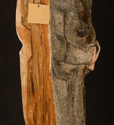 Zdjęcie nr 27: Stojąca figura Matki Boskiej z Dzieciątkiem reprezentuje przykład przyściennej rzeźby z tyłu wydrążonej. Maria stoi w lekkim kontrapoście, podkreślonym wysunięciem do przodu lewego kolana na niewielkim wzgórku. Prawą ręką podtrzymuje Dzieciątko, w lewej dłoni trzyma jabłko. Madonna ma mocno pociągłą twarz o jasnej karnacji z wysokim czołem, rumianych policzkach, długi, prosty nos i wydatne usta. Jej głowa osadzona jest na długiej szyi. Spod białej chusty ubranej na głowę i opadającej na ramiona widać brązowe włosy. Matka Boska na głowie ma koronę o ostrych, krótkich sterczynach. Nałożony na ciemnooliwkową suknię płaszcz w tym samym kolorze, podbity błękitem, tworzy dwa wałkowate zaokrąglone fałdy na brzuchu Marii, spływając miękkimi fałdami spod lewej ręki oraz festonem spod prawej ręki. Niżej fałdy płaszcza i sukni układają się niemal pionowo, opinając materią lewą nogę. Długa suknia odsłania czubki ciżemek. Dzieciątko zostało ujęte w trzech czwartych w prawo. Obie jego rączki wyciągnięte są przed siebie w stronę trzymanego przez Marię jabłka. Z kolei nóżki są skrzyżowane przy stopach. Jezus ma wyrazistą twarz o jasnej karnacji, małym nosem i wydatnych ustach. Jego głowę otaczają brązowe włosy układające się po bokach w charakterystyczne pukle. Jezus ubrany jest w długą, ciemnooliwkową tunikę odsłaniającą fragmenty stóp z charakterystycznymi mankietami przy rękawach. Szaty Matki Boskiej i Dzieciątka są srebrzone i laserowane.