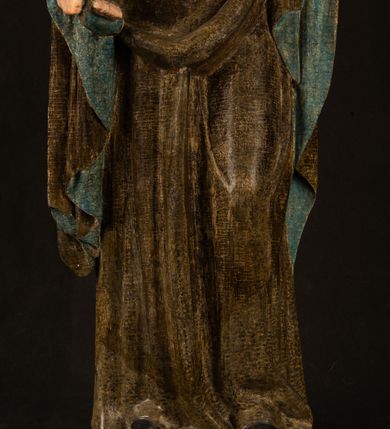 Zdjęcie nr 3: Stojąca figura Matki Boskiej z Dzieciątkiem reprezentuje przykład przyściennej rzeźby z tyłu wydrążonej. Maria stoi w lekkim kontrapoście, podkreślonym wysunięciem do przodu lewego kolana na niewielkim wzgórku. Prawą ręką podtrzymuje Dzieciątko, w lewej dłoni trzyma jabłko. Madonna ma mocno pociągłą twarz o jasnej karnacji z wysokim czołem, rumianych policzkach, długi, prosty nos i wydatne usta. Jej głowa osadzona jest na długiej szyi. Spod białej chusty ubranej na głowę i opadającej na ramiona widać brązowe włosy. Matka Boska na głowie ma koronę o ostrych, krótkich sterczynach. Nałożony na ciemnooliwkową suknię płaszcz w tym samym kolorze, podbity błękitem, tworzy dwa wałkowate zaokrąglone fałdy na brzuchu Marii, spływając miękkimi fałdami spod lewej ręki oraz festonem spod prawej ręki. Niżej fałdy płaszcza i sukni układają się niemal pionowo, opinając materią lewą nogę. Długa suknia odsłania czubki ciżemek. Dzieciątko zostało ujęte w trzech czwartych w prawo. Obie jego rączki wyciągnięte są przed siebie w stronę trzymanego przez Marię jabłka. Z kolei nóżki są skrzyżowane przy stopach. Jezus ma wyrazistą twarz o jasnej karnacji, małym nosem i wydatnych ustach. Jego głowę otaczają brązowe włosy układające się po bokach w charakterystyczne pukle. Jezus ubrany jest w długą, ciemnooliwkową tunikę odsłaniającą fragmenty stóp z charakterystycznymi mankietami przy rękawach. Szaty Matki Boskiej i Dzieciątka są srebrzone i laserowane.