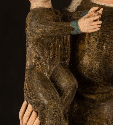 Zdjęcie nr 8: Stojąca figura Matki Boskiej z Dzieciątkiem reprezentuje przykład przyściennej rzeźby z tyłu wydrążonej. Maria stoi w lekkim kontrapoście, podkreślonym wysunięciem do przodu lewego kolana na niewielkim wzgórku. Prawą ręką podtrzymuje Dzieciątko, w lewej dłoni trzyma jabłko. Madonna ma mocno pociągłą twarz o jasnej karnacji z wysokim czołem, rumianych policzkach, długi, prosty nos i wydatne usta. Jej głowa osadzona jest na długiej szyi. Spod białej chusty ubranej na głowę i opadającej na ramiona widać brązowe włosy. Matka Boska na głowie ma koronę o ostrych, krótkich sterczynach. Nałożony na ciemnooliwkową suknię płaszcz w tym samym kolorze, podbity błękitem, tworzy dwa wałkowate zaokrąglone fałdy na brzuchu Marii, spływając miękkimi fałdami spod lewej ręki oraz festonem spod prawej ręki. Niżej fałdy płaszcza i sukni układają się niemal pionowo, opinając materią lewą nogę. Długa suknia odsłania czubki ciżemek. Dzieciątko zostało ujęte w trzech czwartych w prawo. Obie jego rączki wyciągnięte są przed siebie w stronę trzymanego przez Marię jabłka. Z kolei nóżki są skrzyżowane przy stopach. Jezus ma wyrazistą twarz o jasnej karnacji, małym nosem i wydatnych ustach. Jego głowę otaczają brązowe włosy układające się po bokach w charakterystyczne pukle. Jezus ubrany jest w długą, ciemnooliwkową tunikę odsłaniającą fragmenty stóp z charakterystycznymi mankietami przy rękawach. Szaty Matki Boskiej i Dzieciątka są srebrzone i laserowane.
