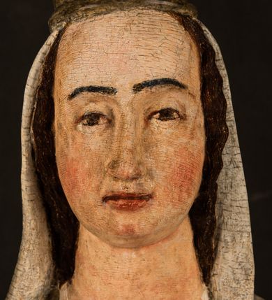 Zdjęcie nr 17: Stojąca figura Matki Boskiej z Dzieciątkiem reprezentuje przykład przyściennej rzeźby z tyłu wydrążonej. Maria stoi w lekkim kontrapoście, podkreślonym wysunięciem do przodu lewego kolana na niewielkim wzgórku. Prawą ręką podtrzymuje Dzieciątko, w lewej dłoni trzyma jabłko. Madonna ma mocno pociągłą twarz o jasnej karnacji z wysokim czołem, rumianych policzkach, długi, prosty nos i wydatne usta. Jej głowa osadzona jest na długiej szyi. Spod białej chusty ubranej na głowę i opadającej na ramiona widać brązowe włosy. Matka Boska na głowie ma koronę o ostrych, krótkich sterczynach. Nałożony na ciemnooliwkową suknię płaszcz w tym samym kolorze, podbity błękitem, tworzy dwa wałkowate zaokrąglone fałdy na brzuchu Marii, spływając miękkimi fałdami spod lewej ręki oraz festonem spod prawej ręki. Niżej fałdy płaszcza i sukni układają się niemal pionowo, opinając materią lewą nogę. Długa suknia odsłania czubki ciżemek. Dzieciątko zostało ujęte w trzech czwartych w prawo. Obie jego rączki wyciągnięte są przed siebie w stronę trzymanego przez Marię jabłka. Z kolei nóżki są skrzyżowane przy stopach. Jezus ma wyrazistą twarz o jasnej karnacji, małym nosem i wydatnych ustach. Jego głowę otaczają brązowe włosy układające się po bokach w charakterystyczne pukle. Jezus ubrany jest w długą, ciemnooliwkową tunikę odsłaniającą fragmenty stóp z charakterystycznymi mankietami przy rękawach. Szaty Matki Boskiej i Dzieciątka są srebrzone i laserowane.